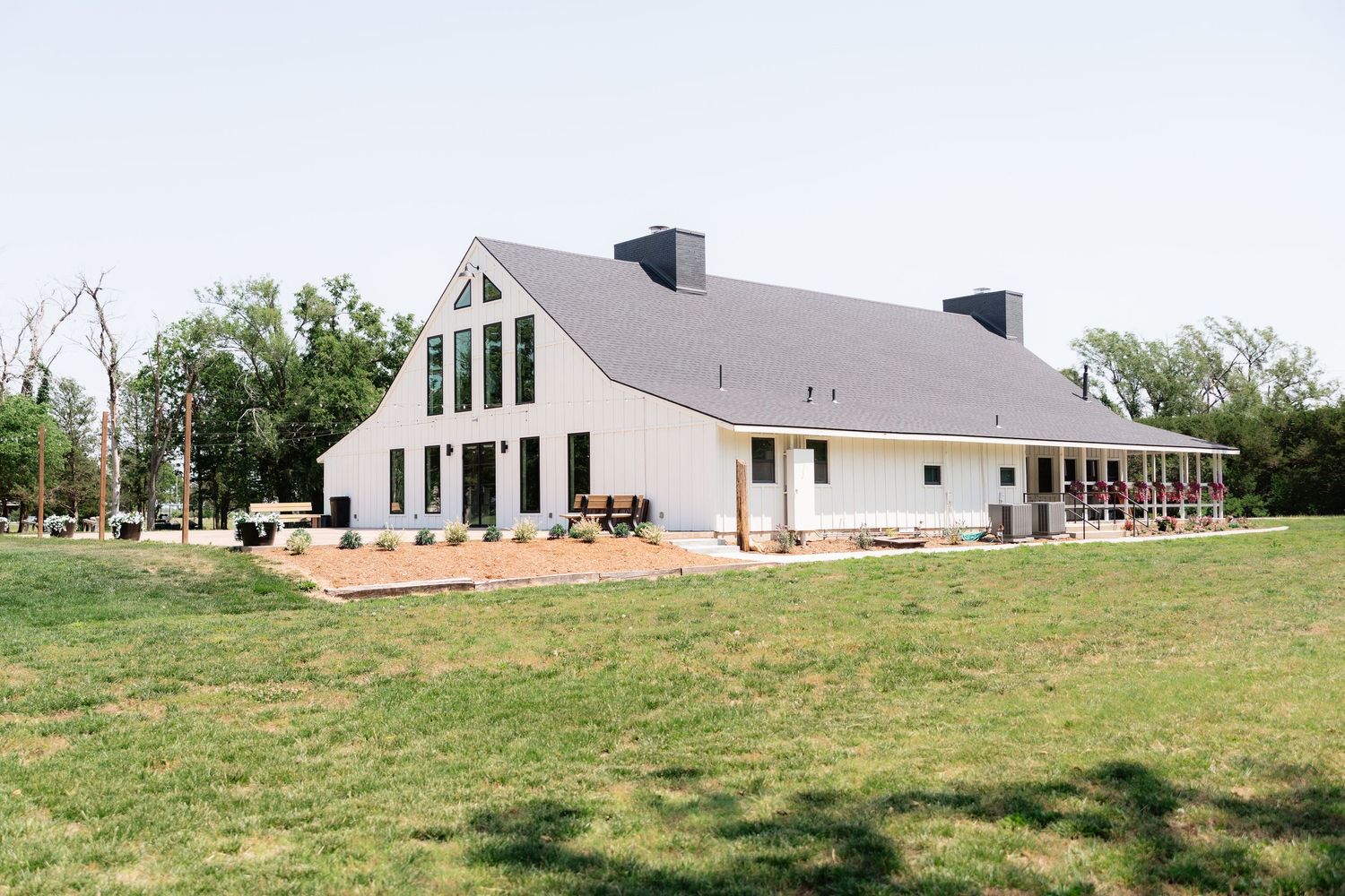 Modern white barn wedding venue with large windows and manicured lawn on sunny day.