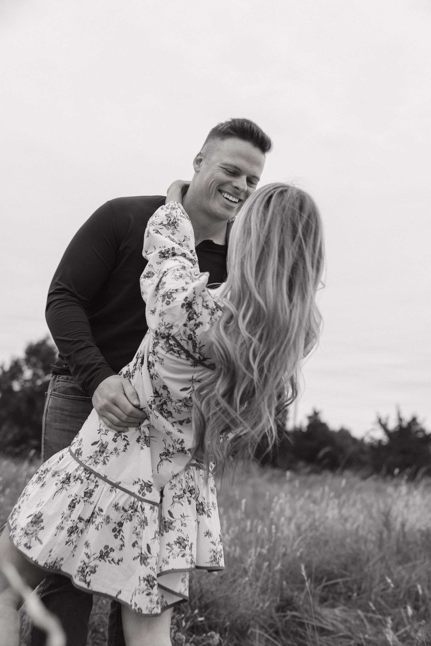 Black and white photo of a laughing couple dancing in an open grassy field.