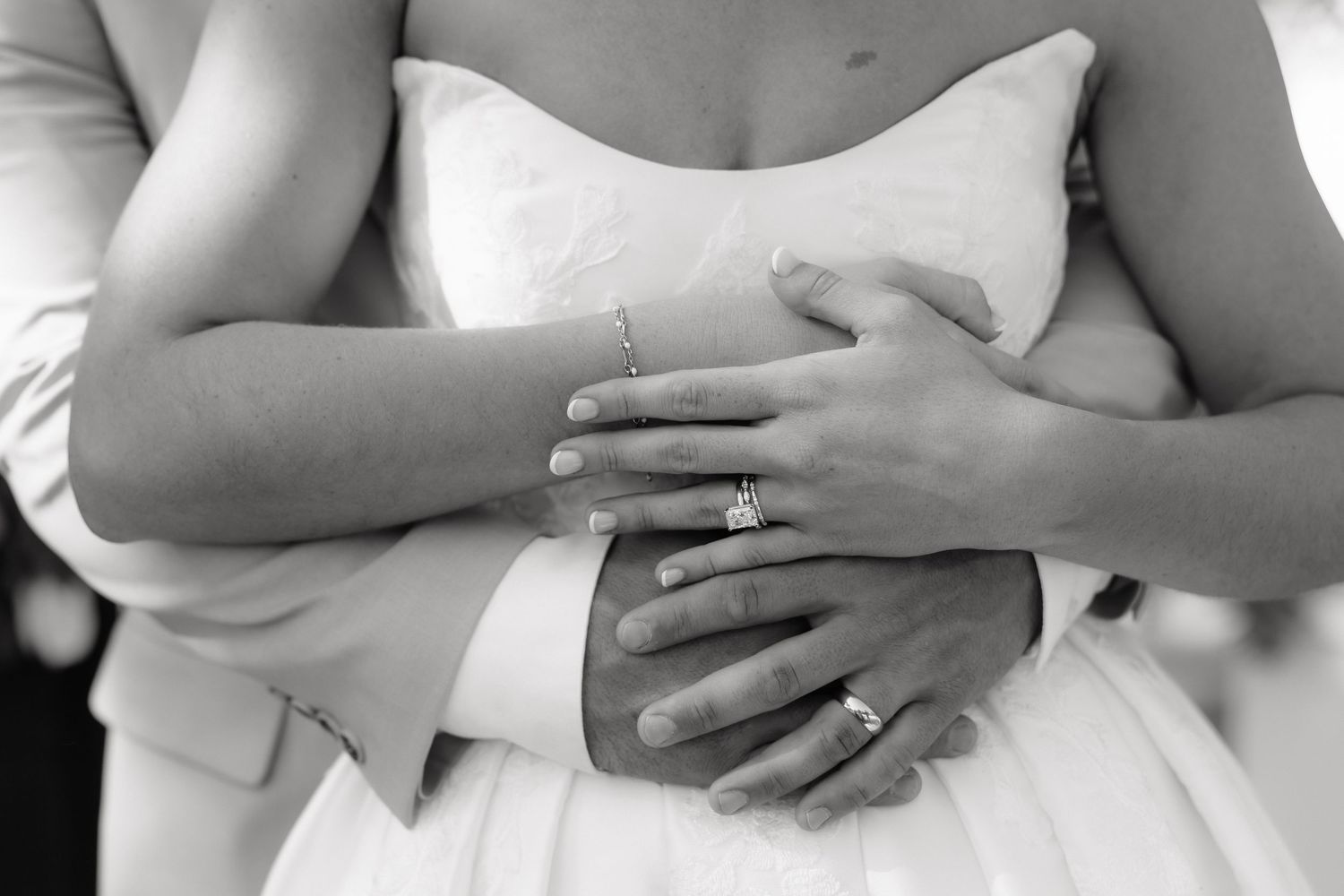Black and white close-up of bride and groom embracing, showcasing elegant diamond engagement and wedding rings.