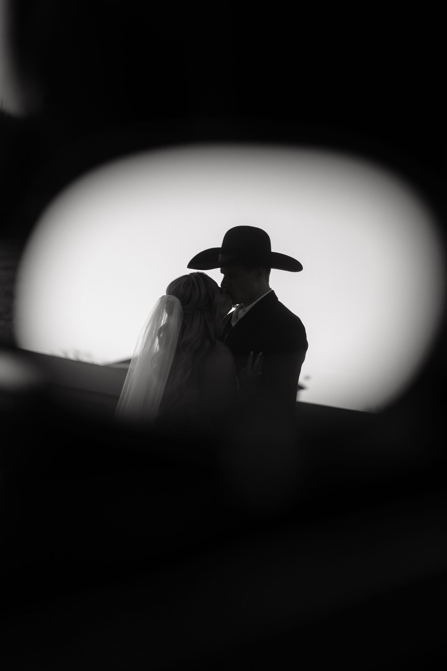 Silhouette of a bride and groom sharing a romantic moment, with the groom wearing a cowboy hat, in black and white.