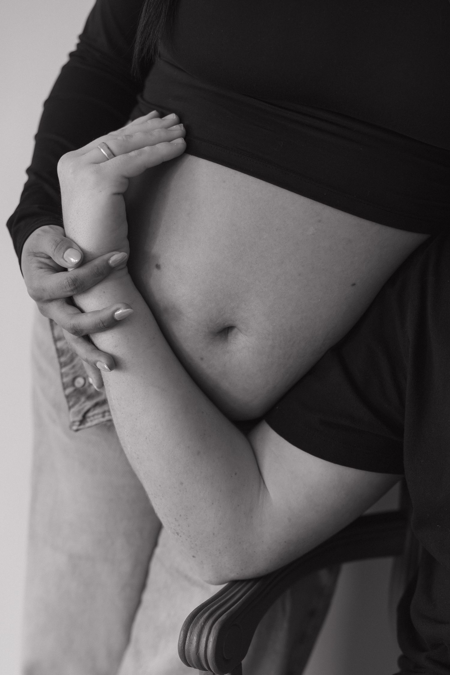Black and white close-up of a pregnant woman cradling her baby bump with both hands.