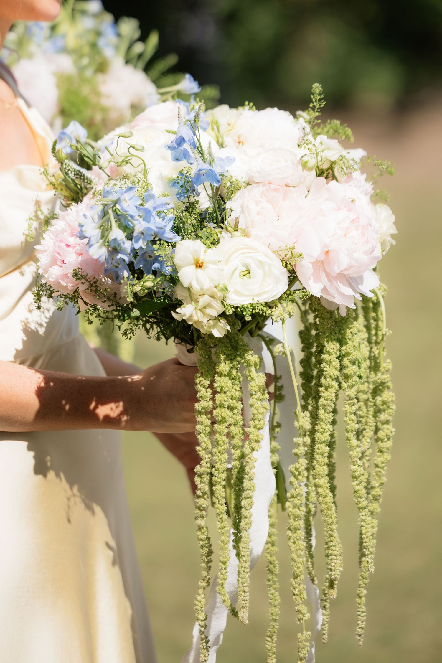 Bridesmaid holds lush bouquet of pink peonies, blue hydrangeas, and cascading green amaranthus.