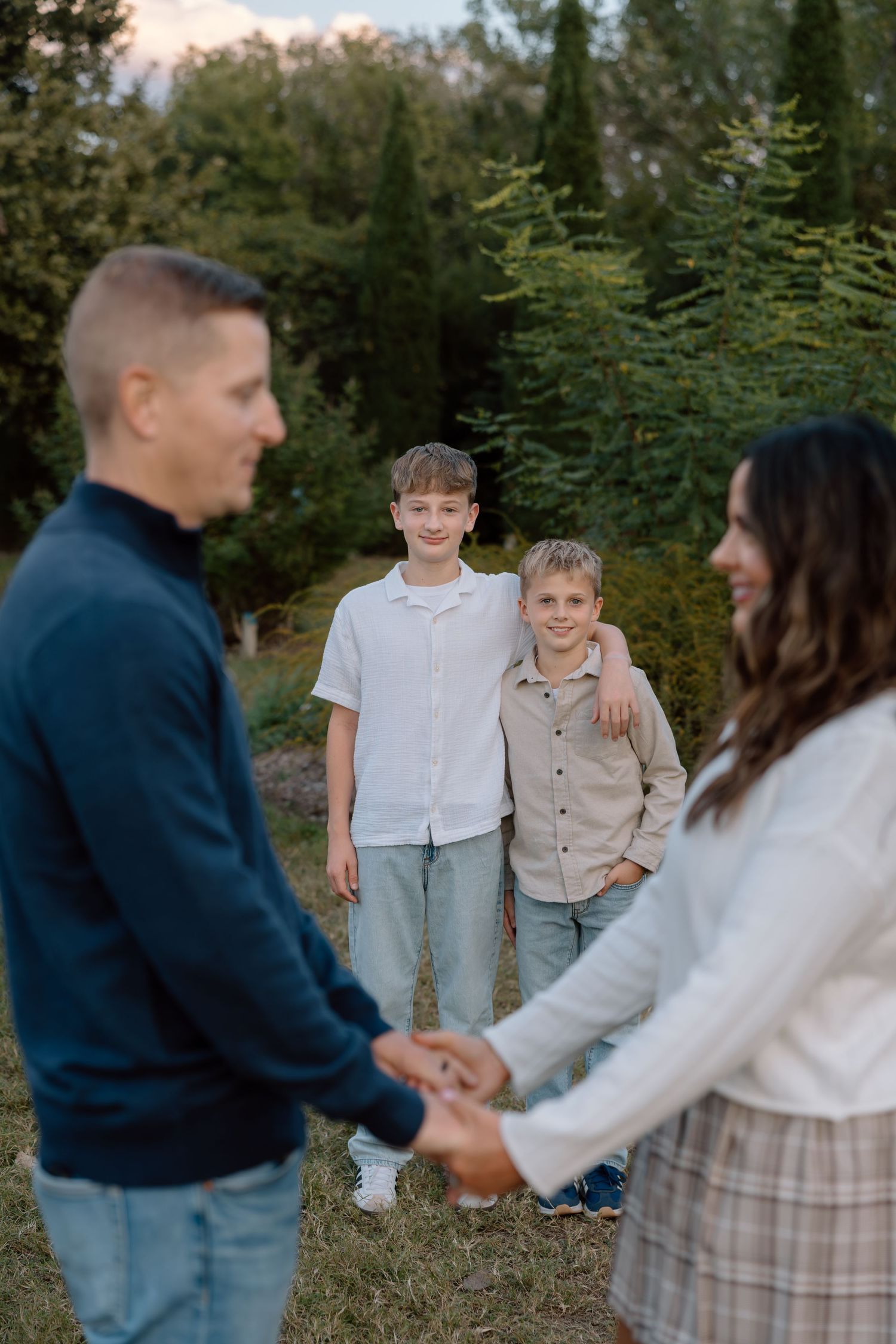 Two young brothers smiling as their parents hold hands in the foreground during family photoshoot.