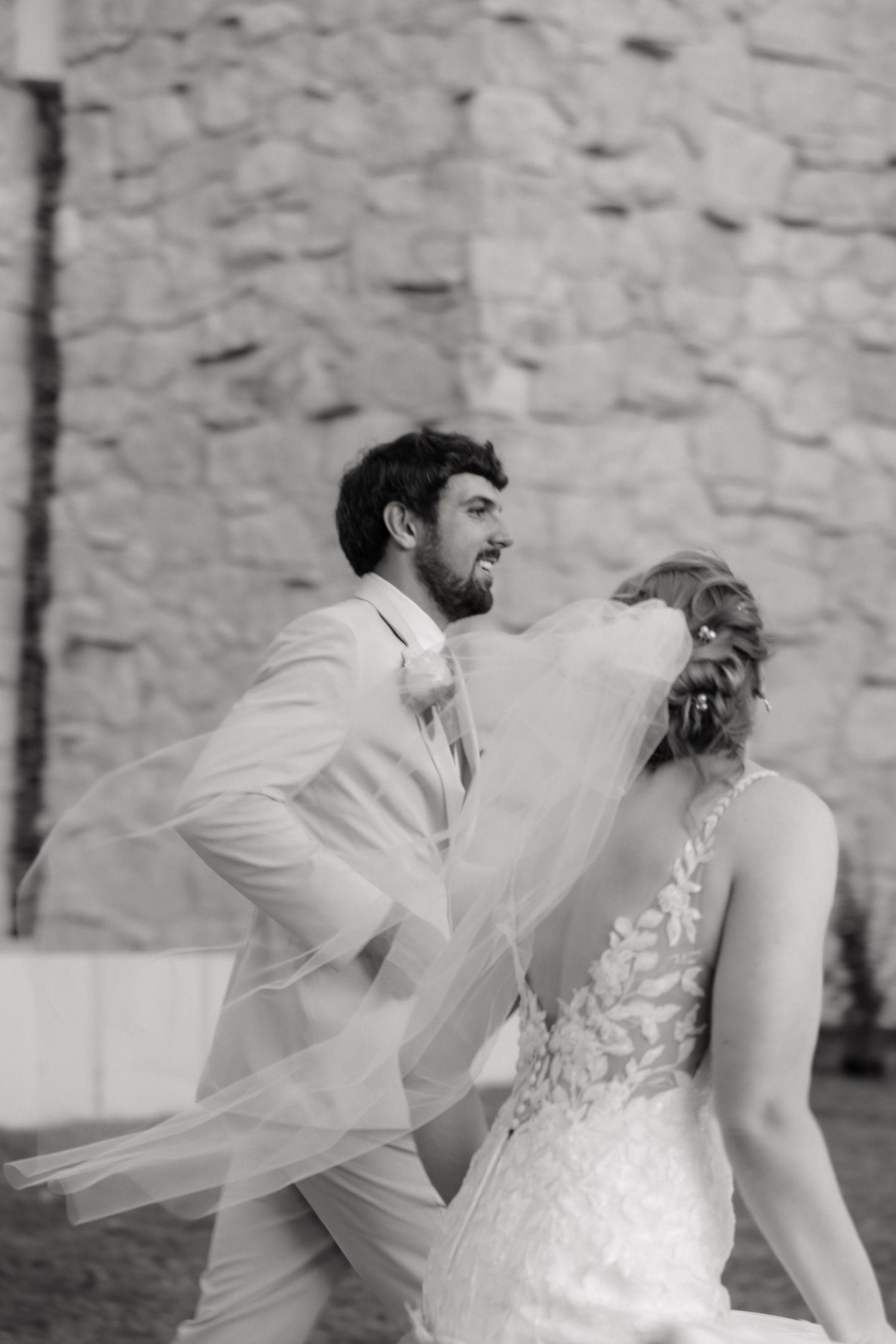 Black and white photo of bride and groom walking with veil blowing wind.