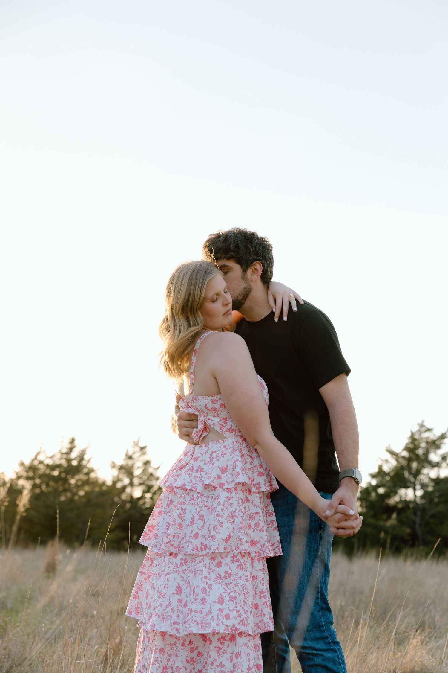 Romantic couple sharing a tender kiss in a sunlit golden field, woman wearing a pink floral dress.