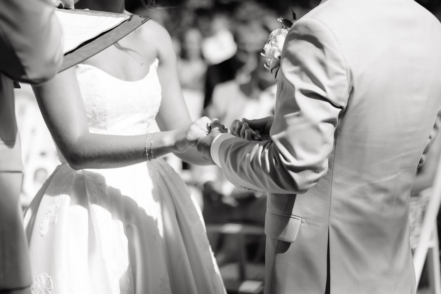 Black and white photo of bride and groom exchanging rings during outdoor wedding ceremony.
