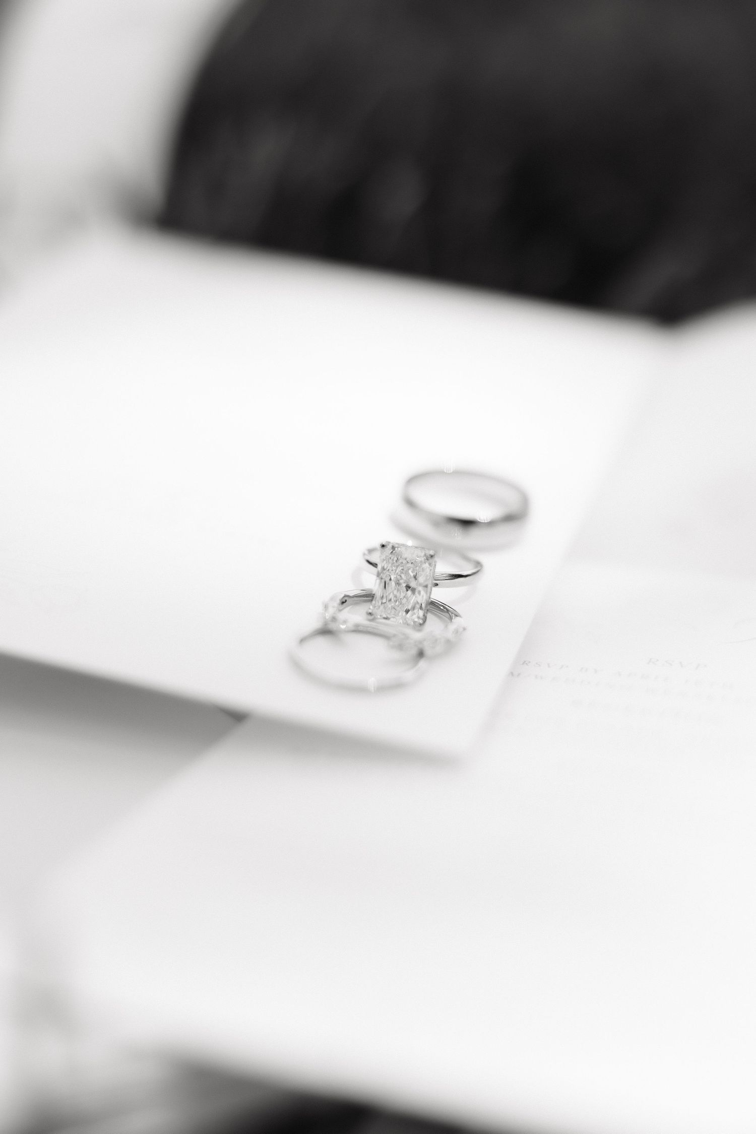 Black and white close-up of elegant diamond engagement ring and wedding bands on white fabric.