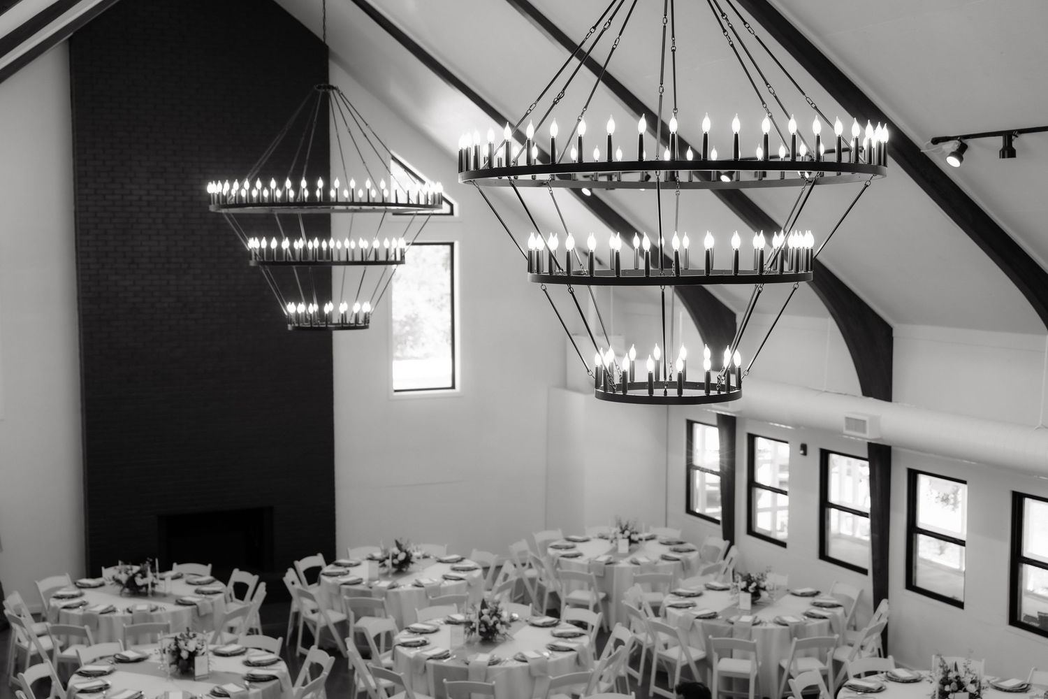 Black and white photo of an elegant wedding reception venue with dramatic chandelier lighting and round tables.