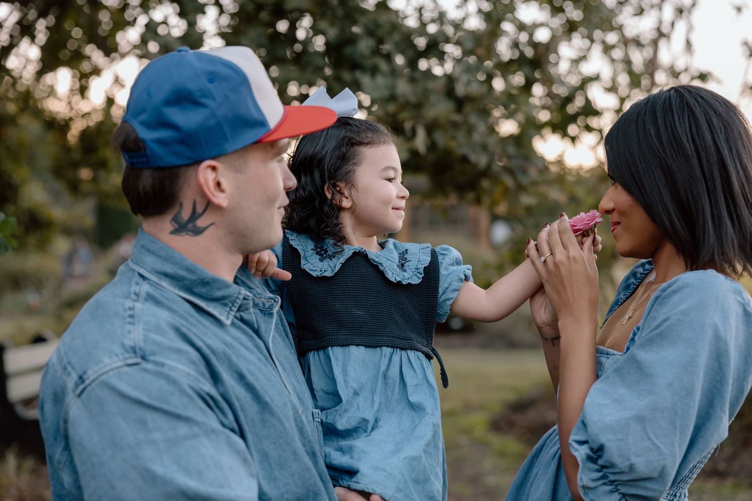 A young interracial family in matching denim outfits shares a sweet moment with their daughter outdoors.