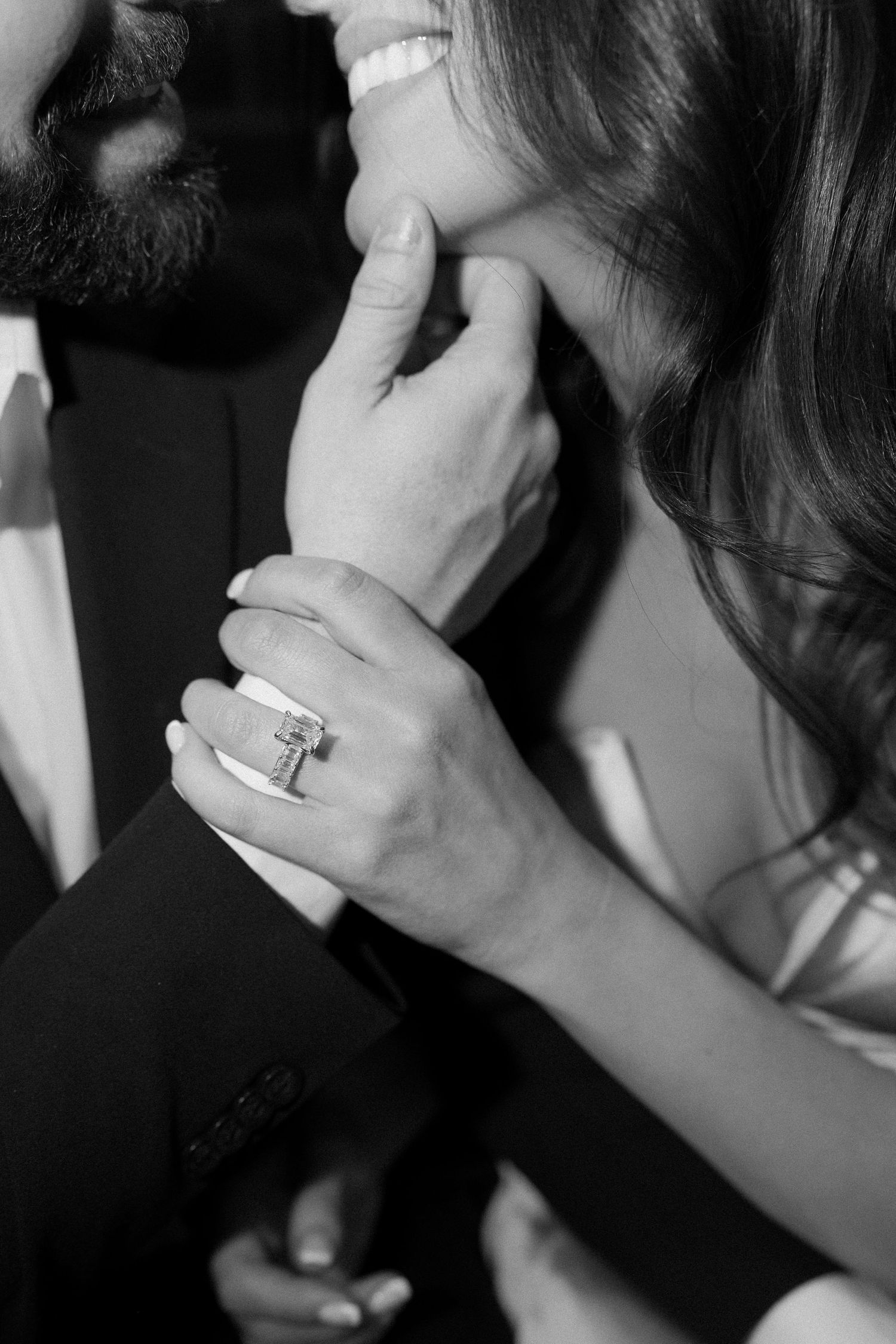 Black and white close-up of couple almost kissing, featuring a stunning emerald-cut diamond engagement ring.