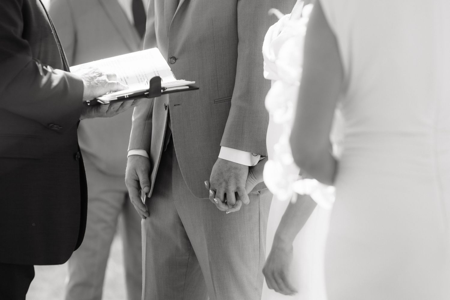 Officiant reads vows as groom holds bride's hand during intimate wedding ceremony.