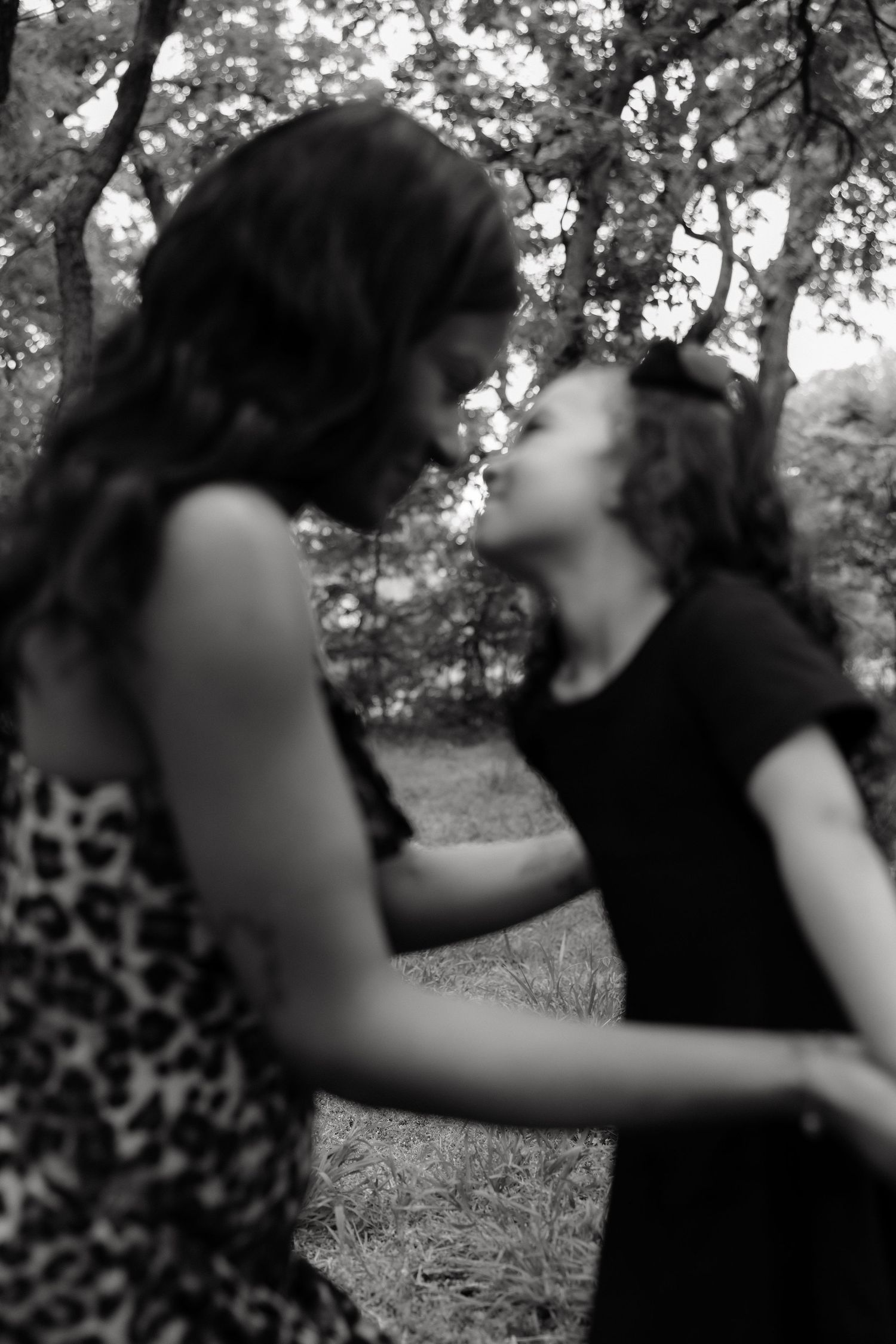 Black and white photo of a woman and young girl sharing a tender moment in a wooded outdoor setting.