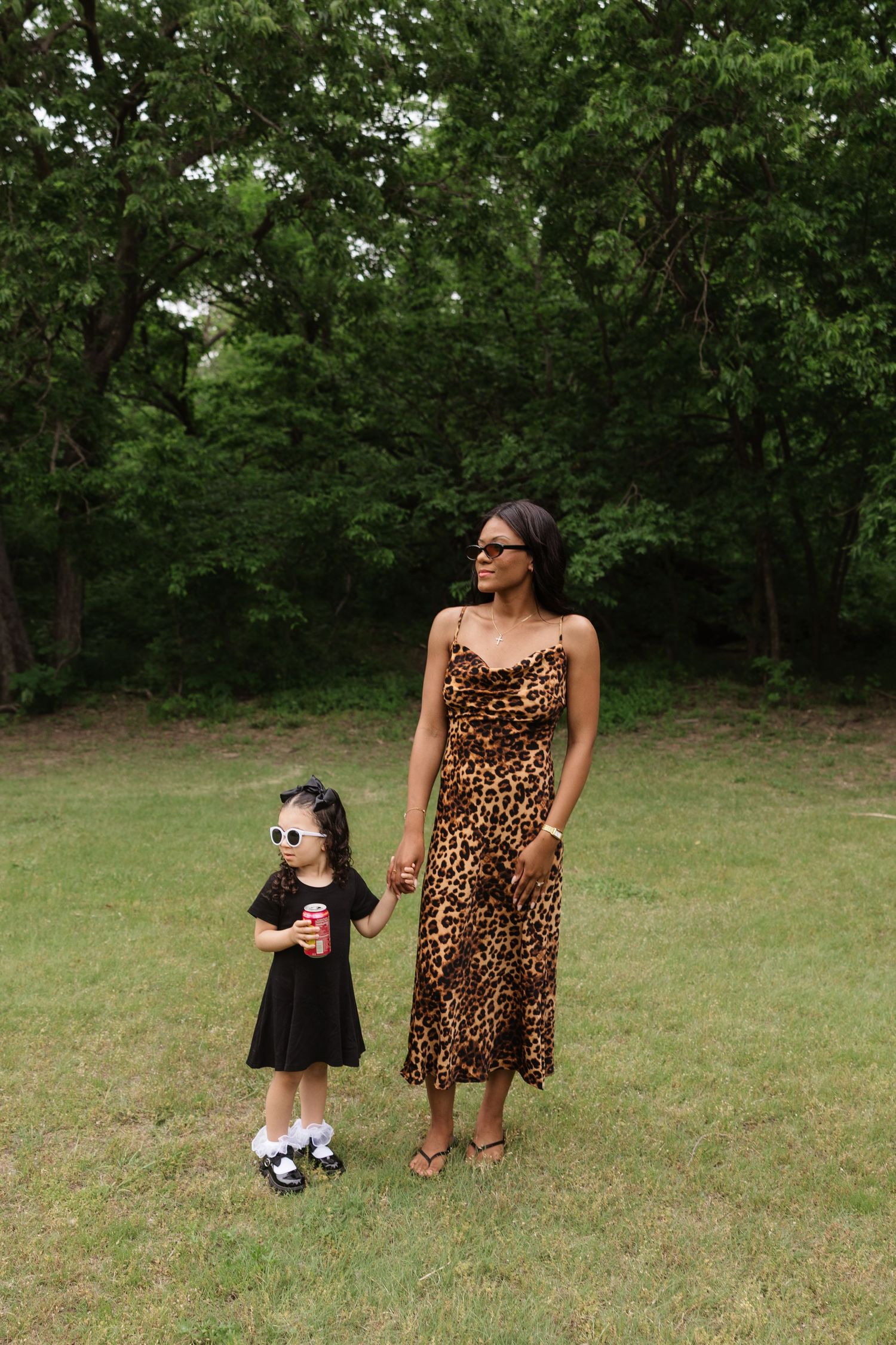 Mother in leopard print dress holding hands with young daughter in a park.