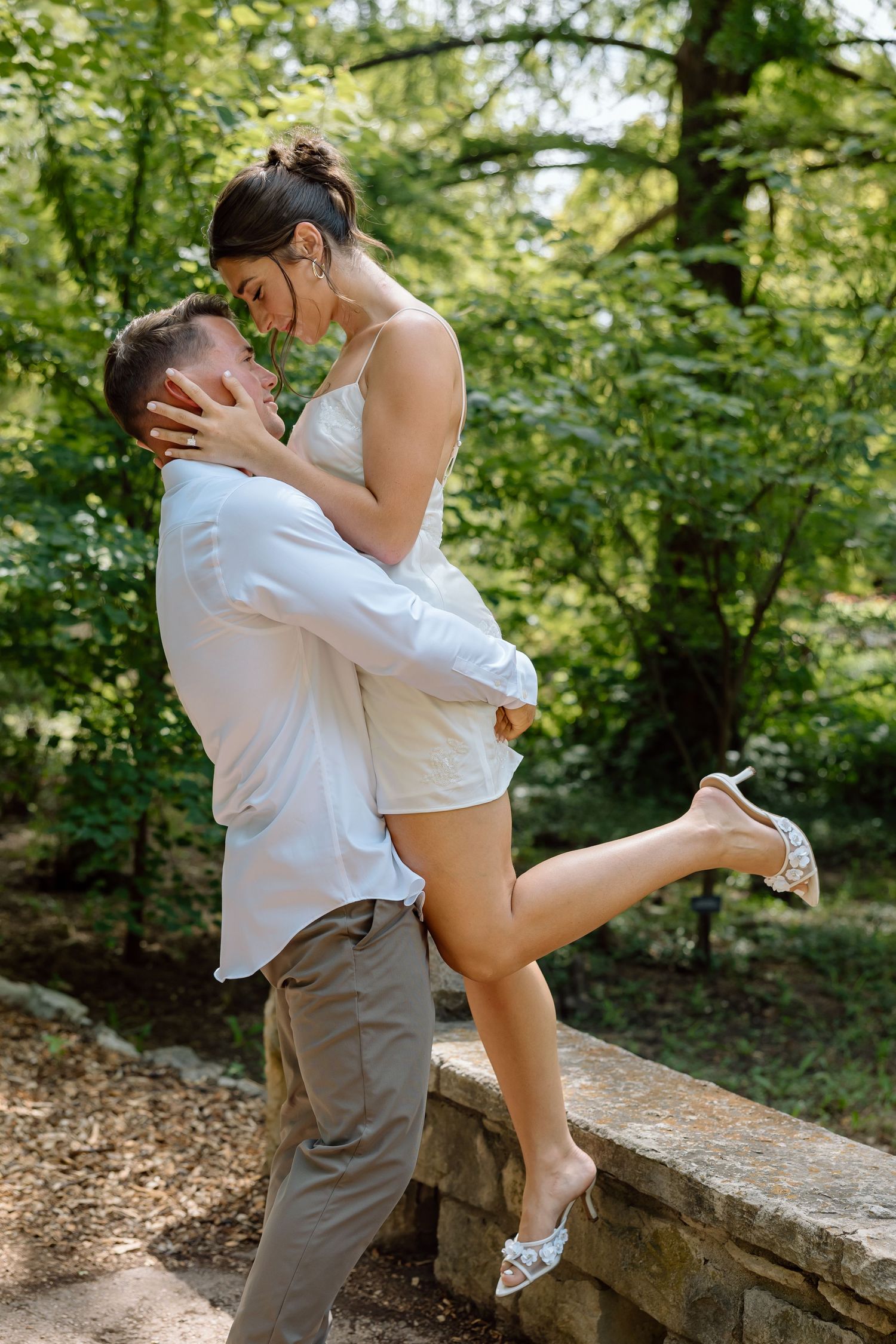 Romantic couple sharing a tender moment as man lifts woman in a lush green park.