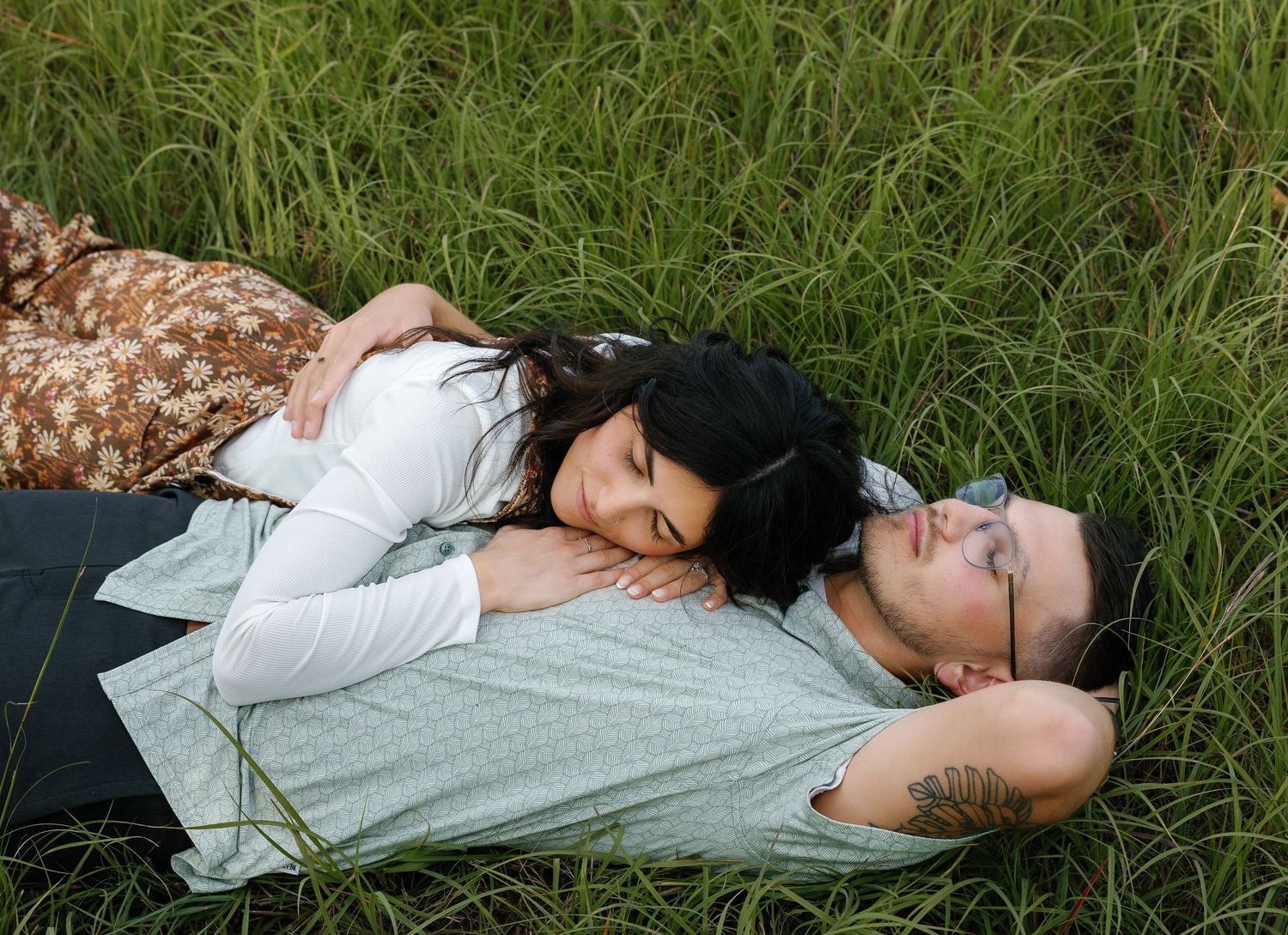 Romantic couple lying in tall green grass, woman resting her head on mans chest peacefully.