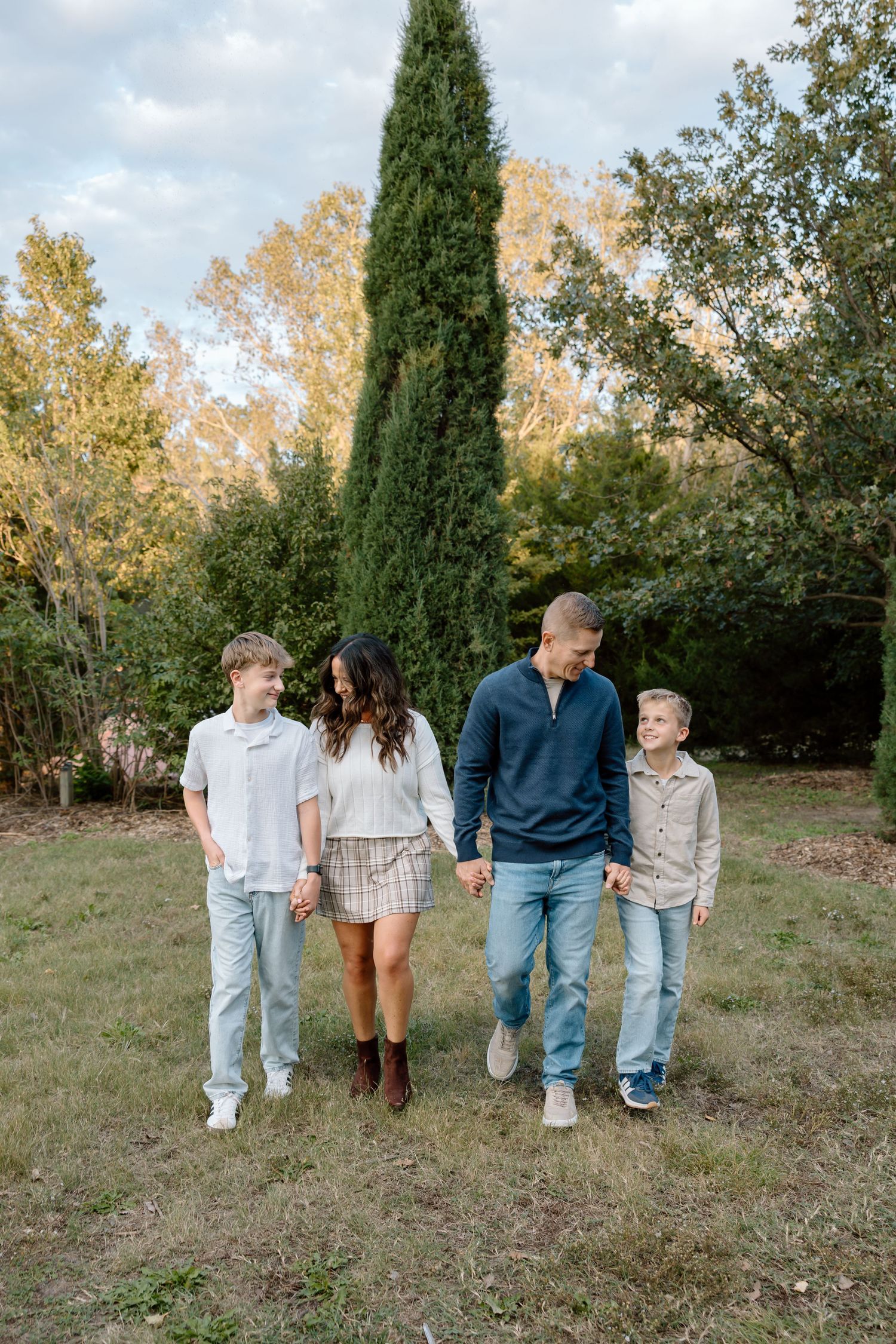 Family of four walking hand-in-hand through a lush green outdoor setting during golden hour.