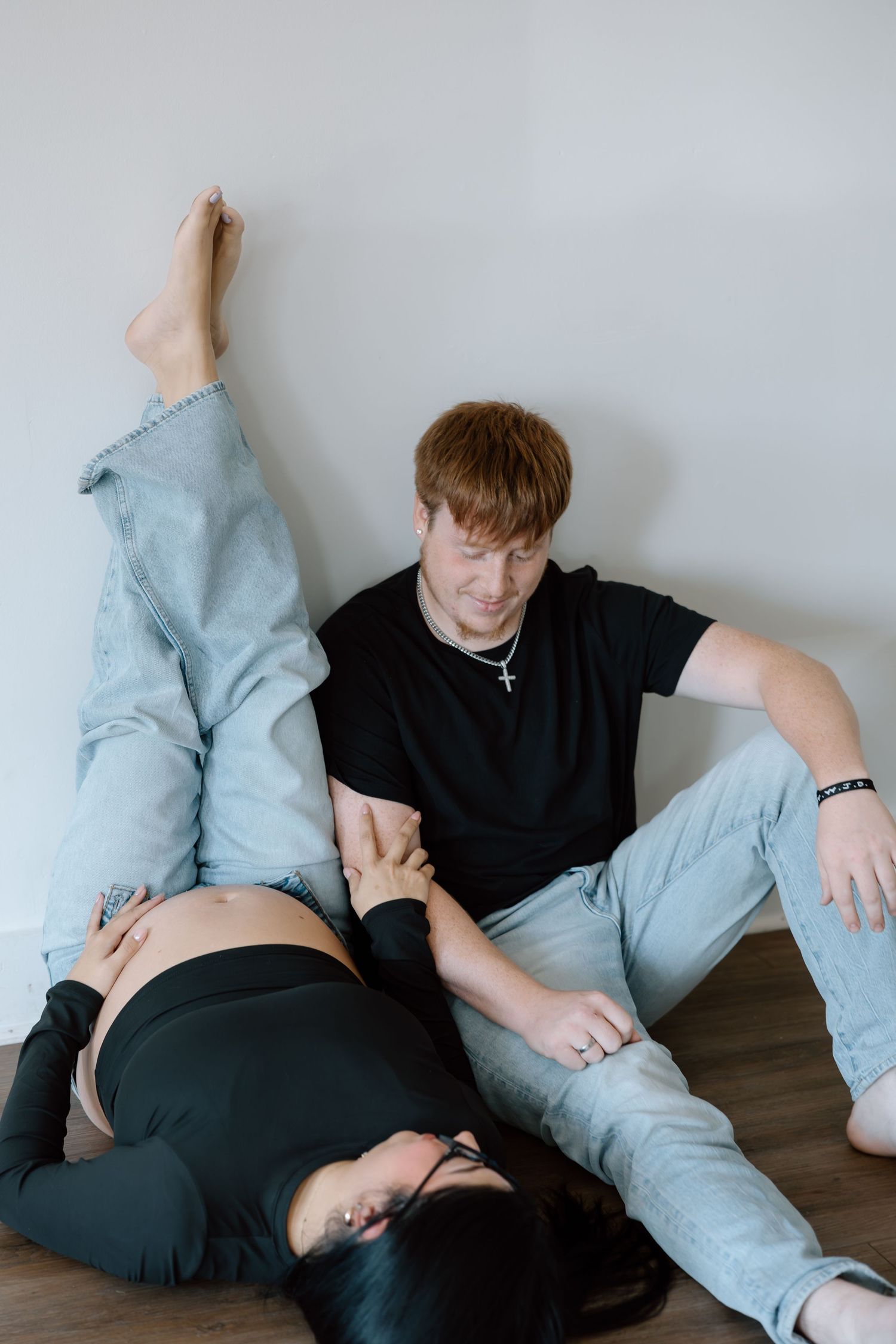 Couple sharing a tender moment on the floor, with pregnant woman lying down as partner holds her hand.