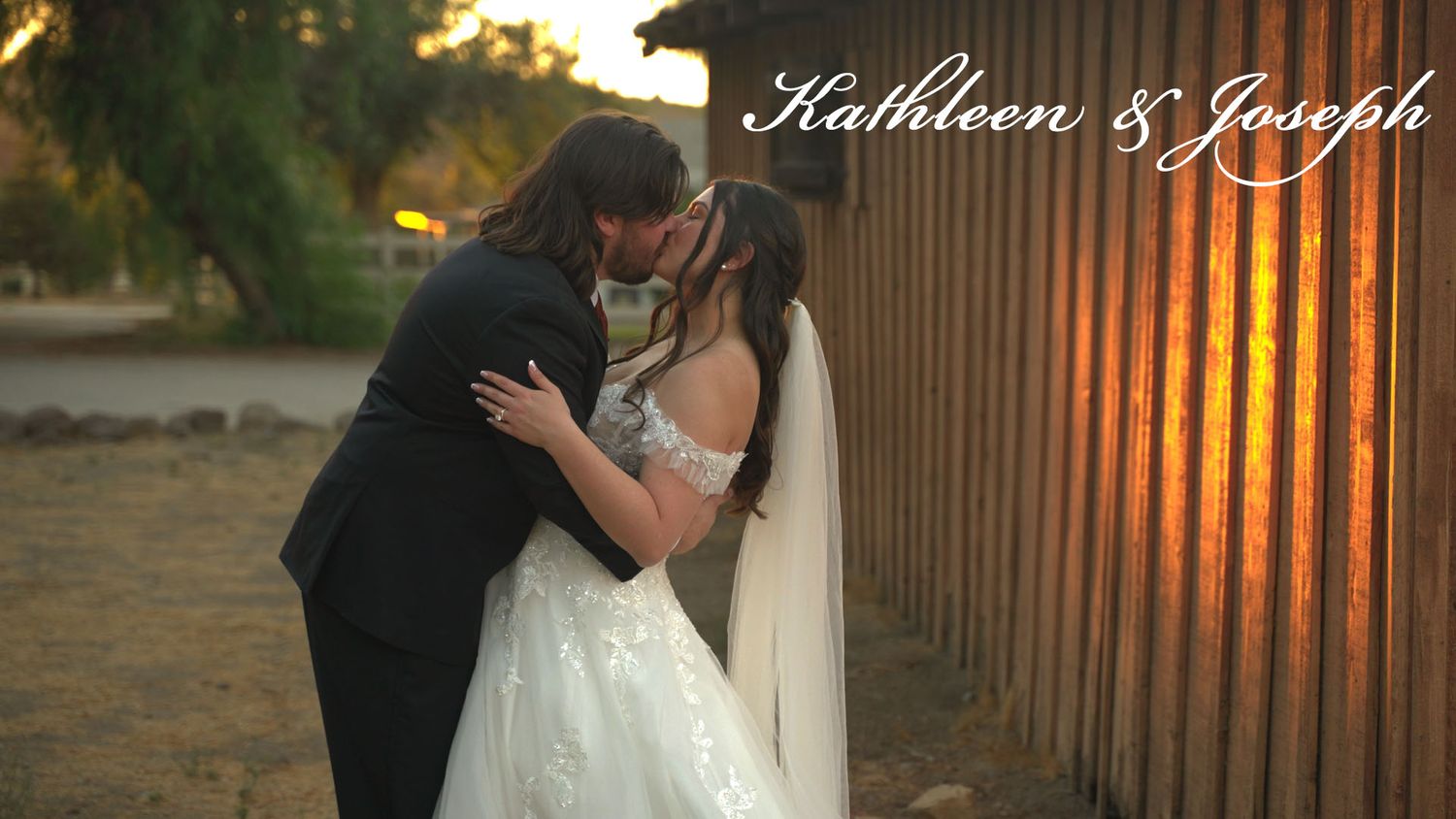 Intimate wedding moment captured at sunset with wooden fence background.