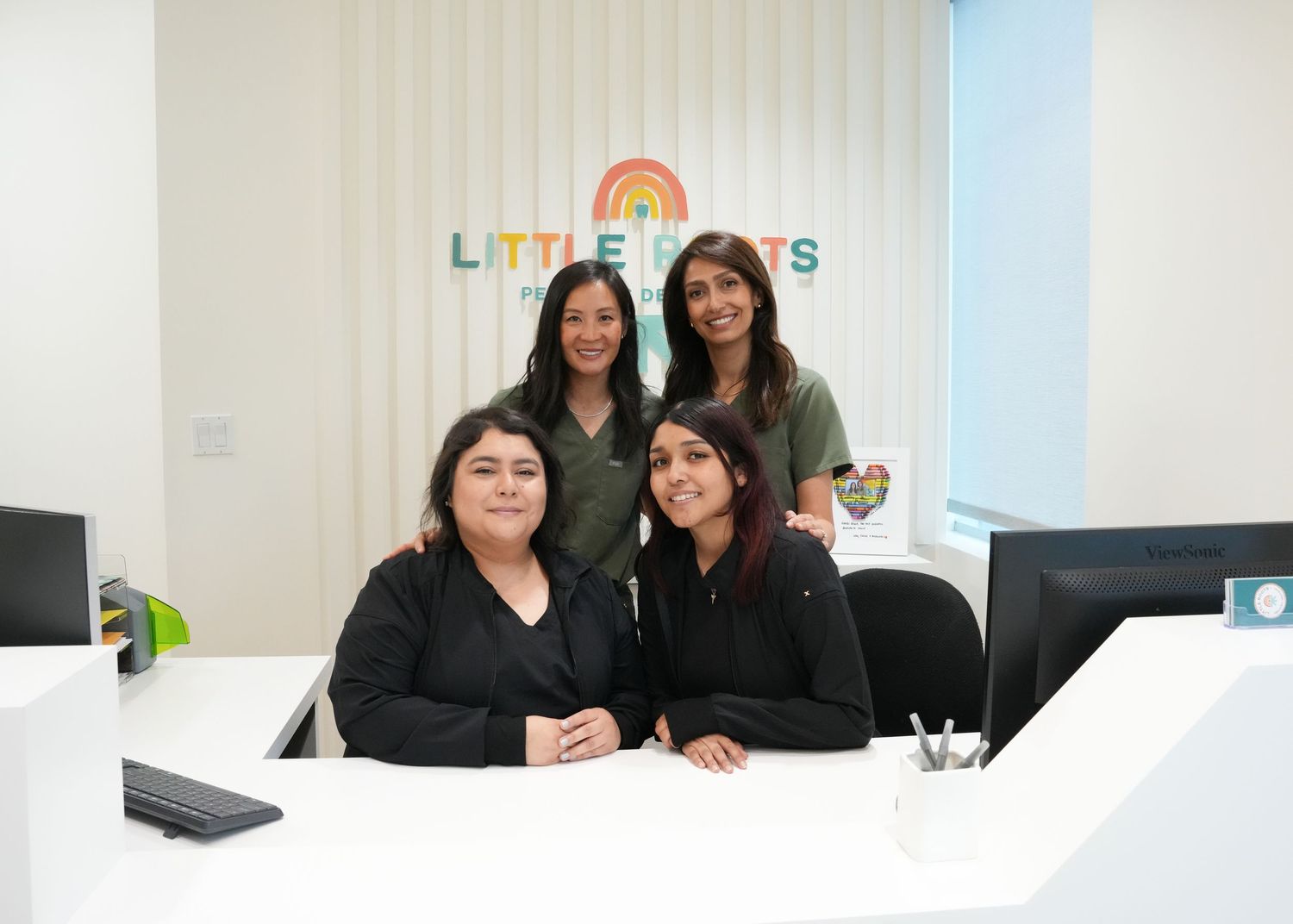 Four people sitting at desks in modern office with colorful rainbow logo on wall.