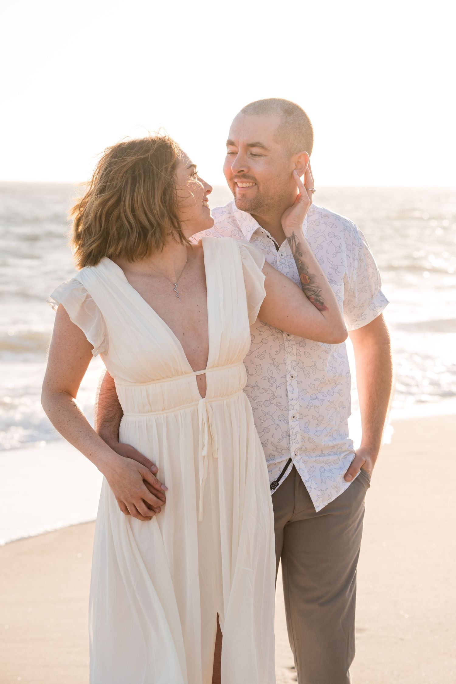 A couple in love shares intimate moments on a sun-drenched beach during a romantic photoshoot at sunset.