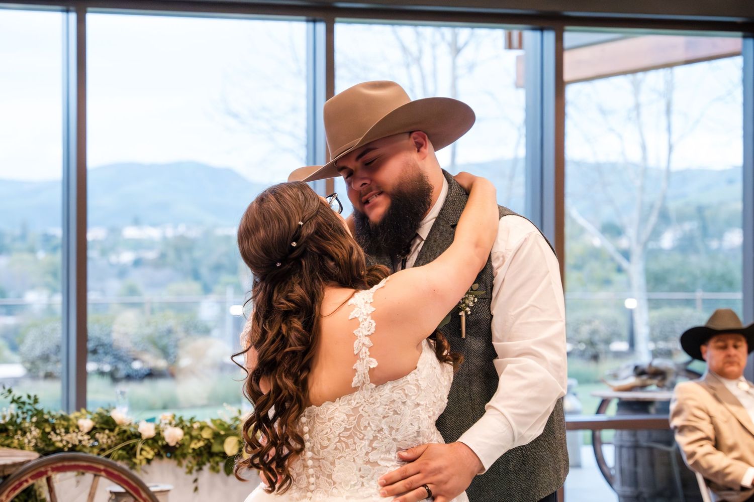 A romantic couple shares kisses at their rustic wedding venue with scenic mountain views through floor-to-ceiling windows.