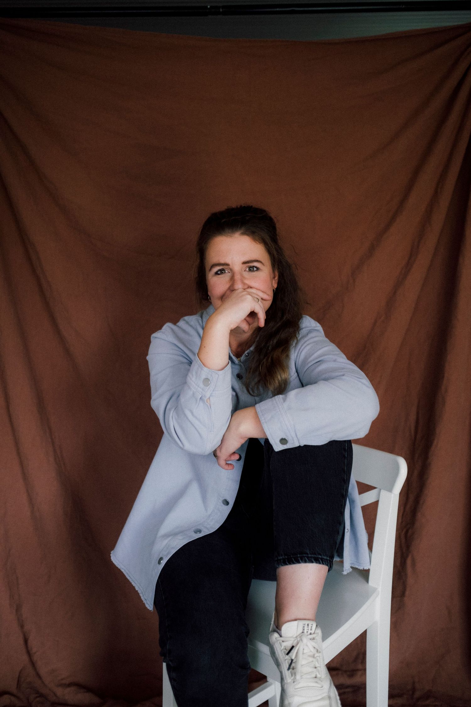 A figure in a gray sweater and black pants sits on a white chair against a brown backdrop in various poses.