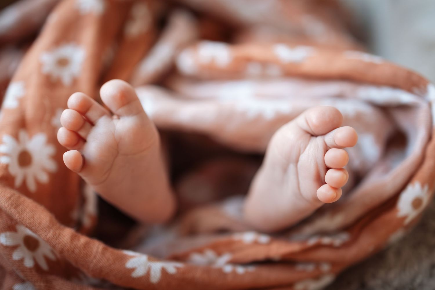 Tiny baby feet wrapped in a soft peach-colored floral blanket in gentle natural lighting.