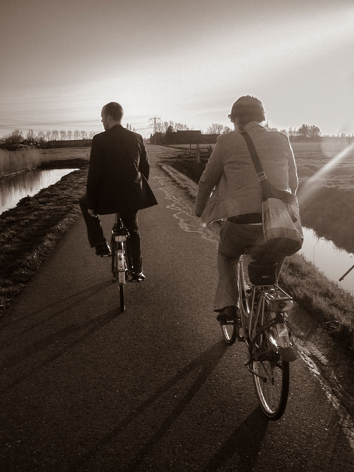 Rear view of a man and woman biking through the rural area of The Netherlands in black and white.