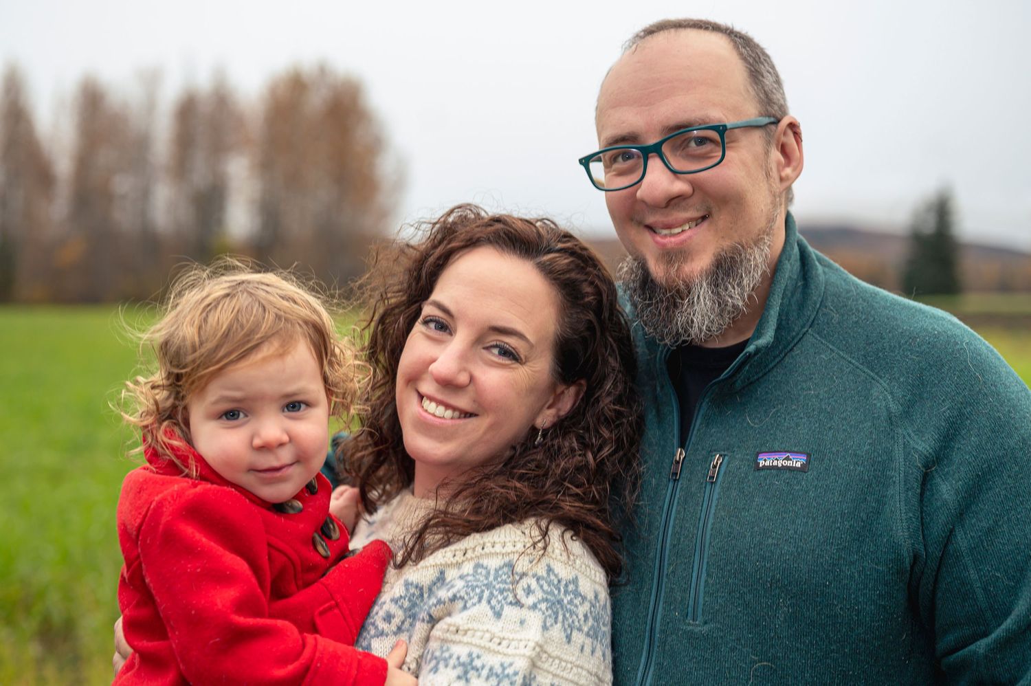A happy family in winter clothing poses together outdoors against a natural landscape background.