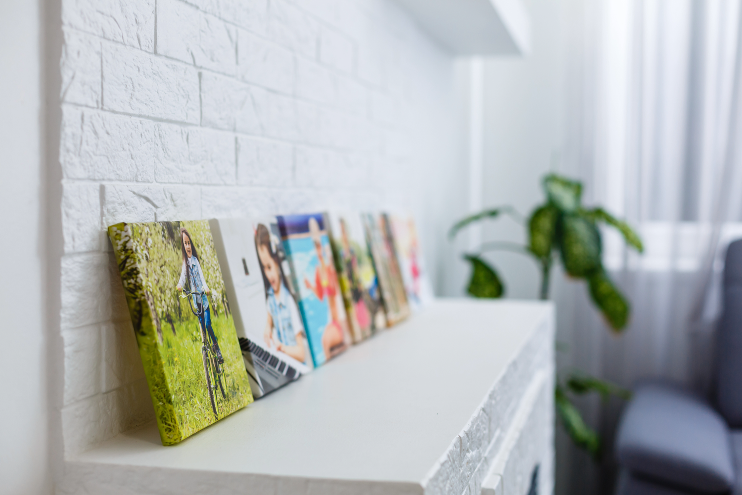 Colorful abstract art canvases displayed on a white floating shelf against a brick wall with houseplant in background.