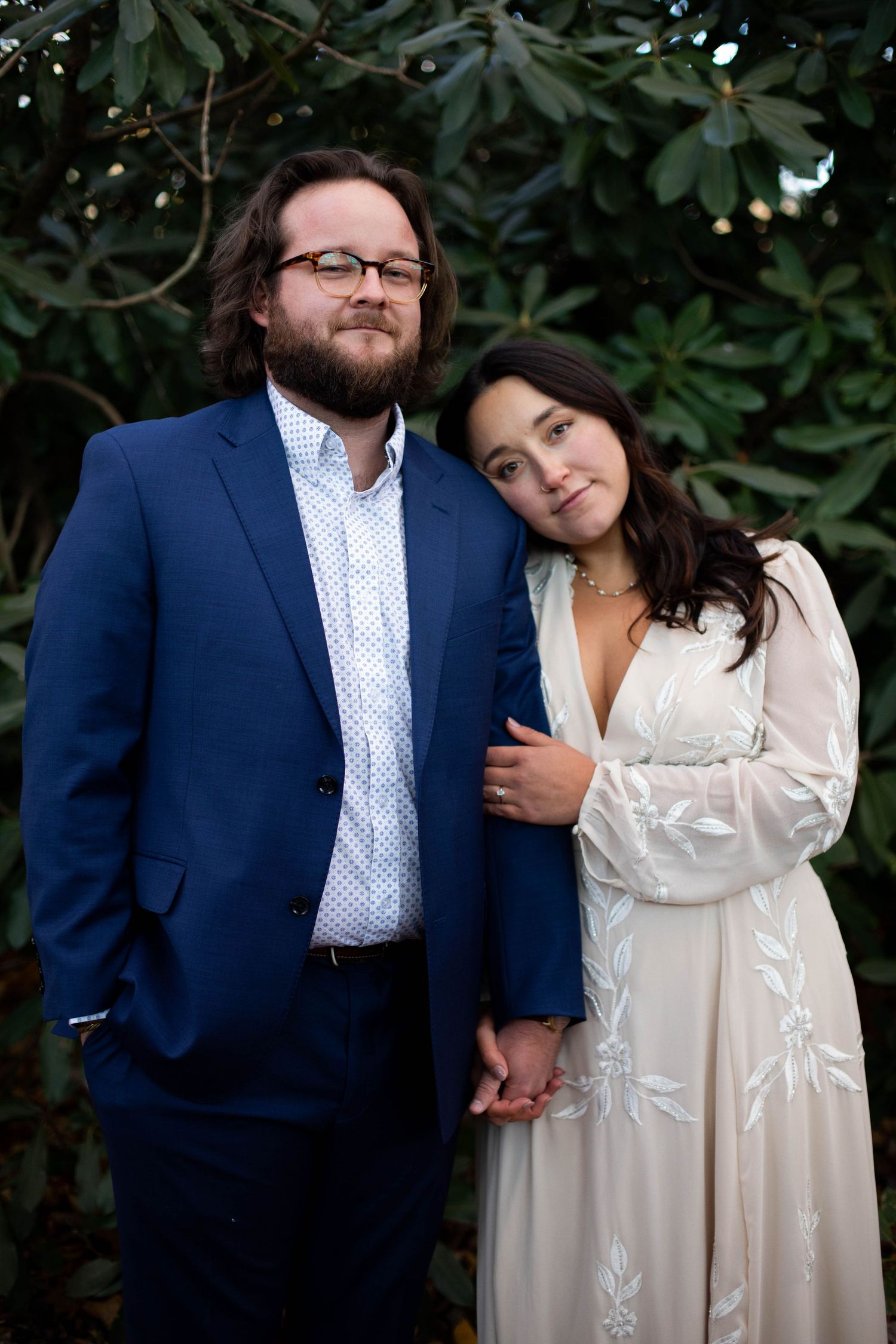 Couple in formal attire sharing intimate moment against dark foliage background.