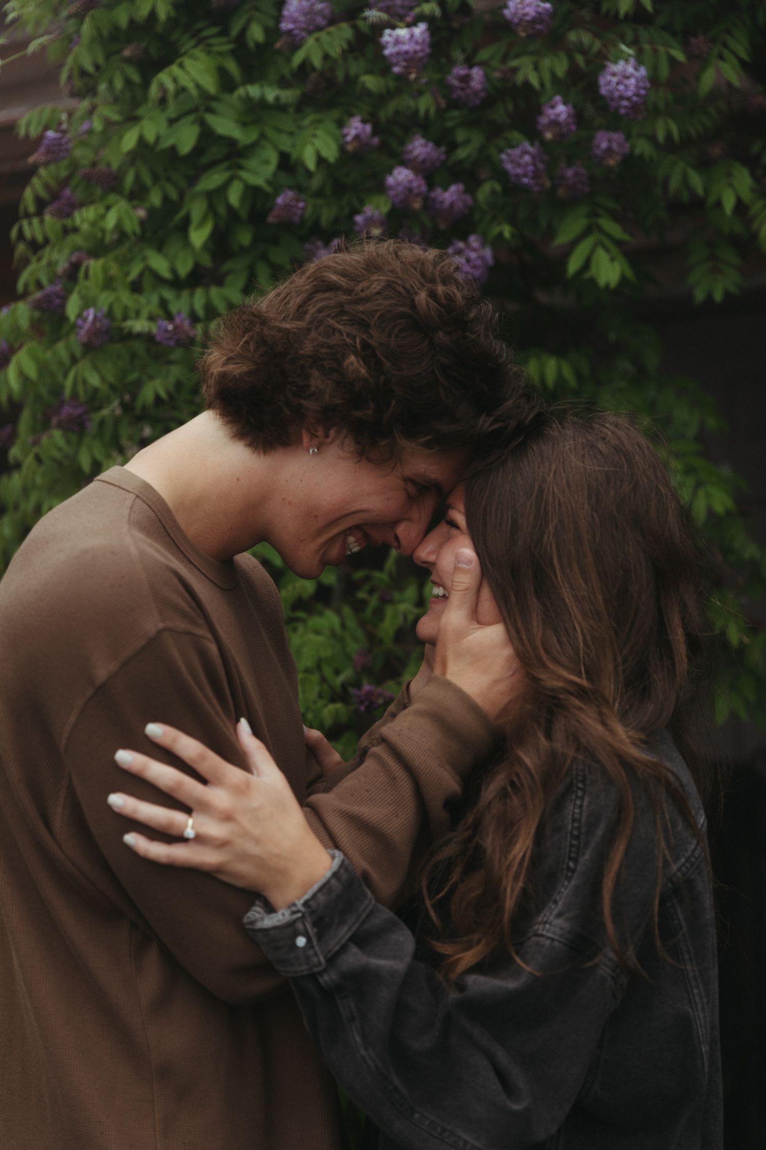 Romantic couple sharing an intimate moment against a backdrop of purple flowers and greenery.
