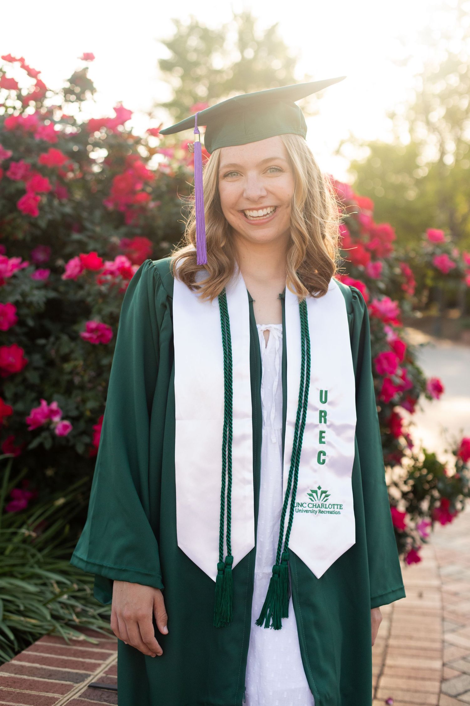 Academic regalia featuring green graduation gown with white stole and honor cords against floral backdrop.