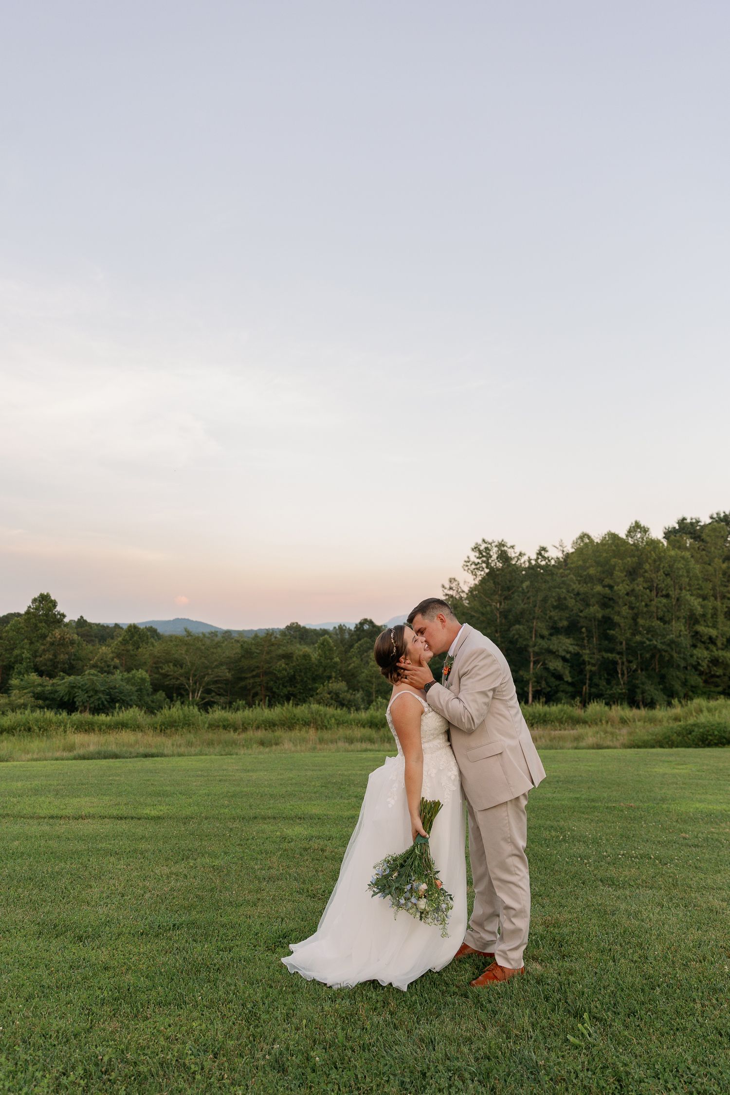 Romantic wedding portrait in a green field during golden hour with mountains in background.