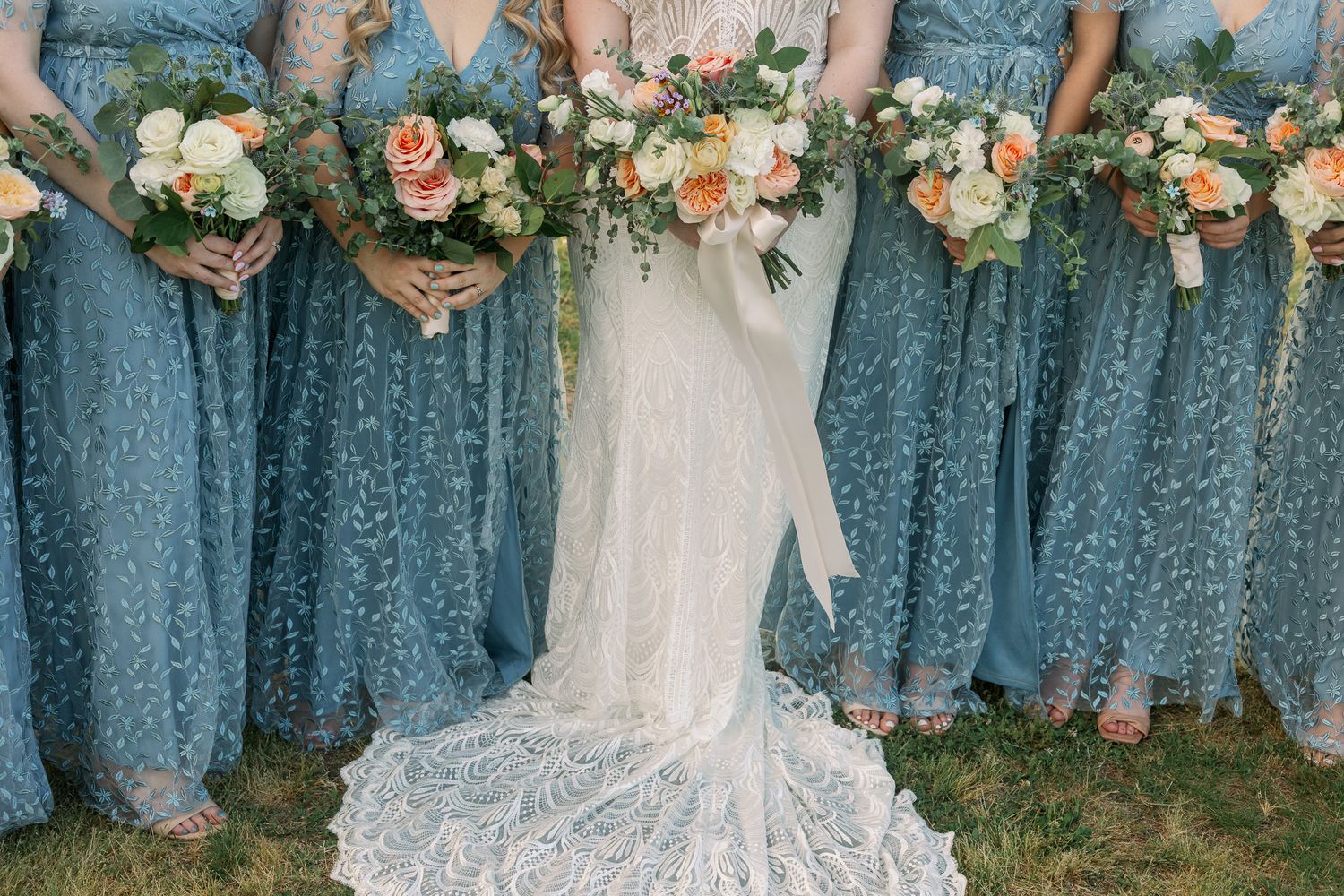 Bridesmaids in matching blue sequined dresses holding floral bouquets at an outdoor wedding.