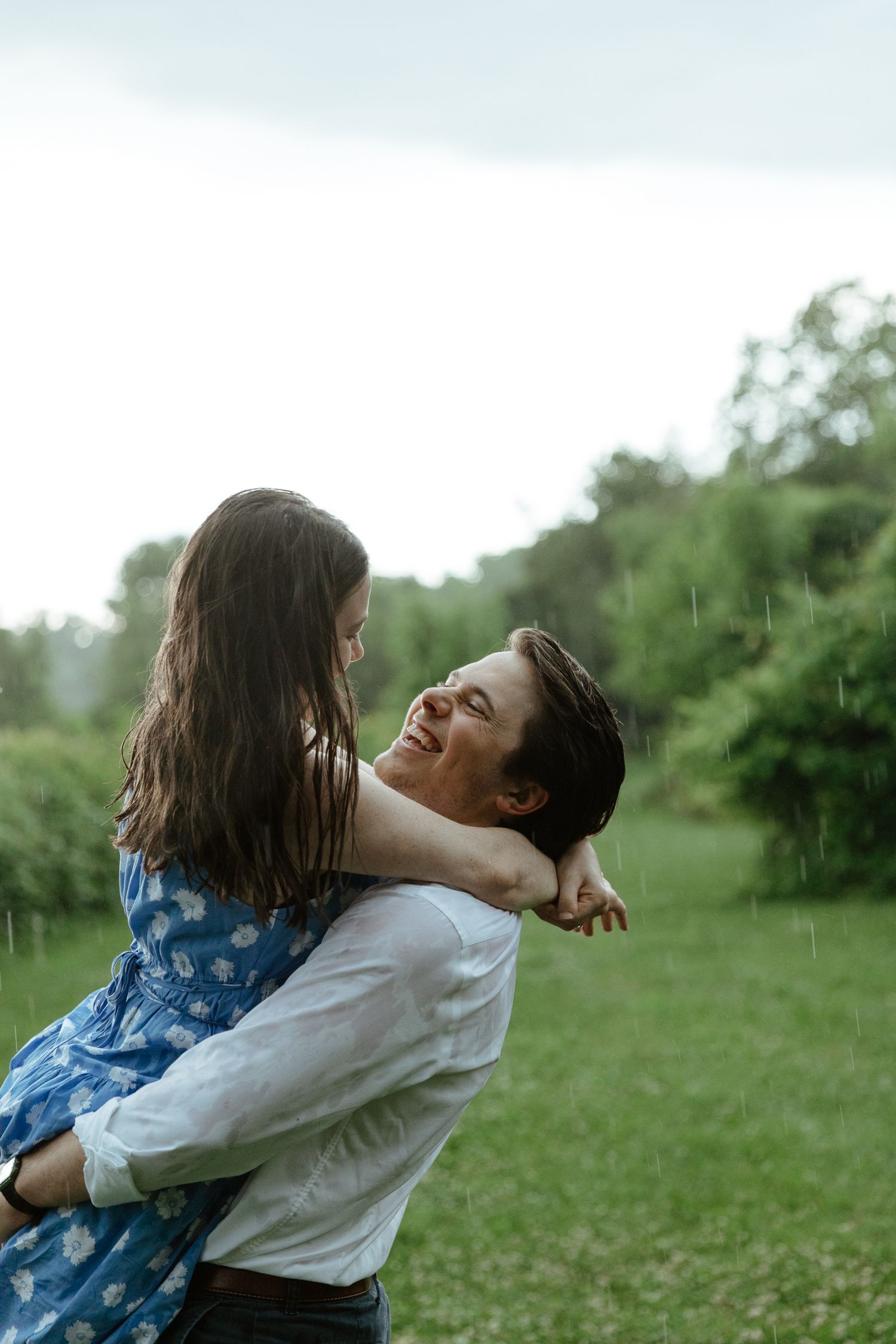 A joyful embrace in a green field during a light rain shower.