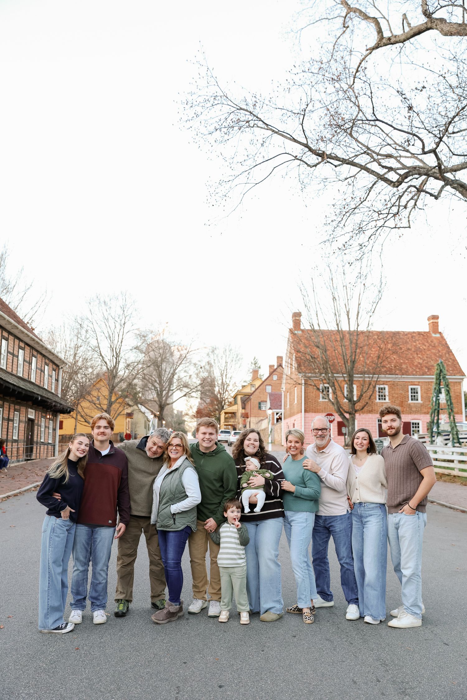 Large family group portrait outdoors on a street, smiling together near historic brick buildings with bare winter trees.