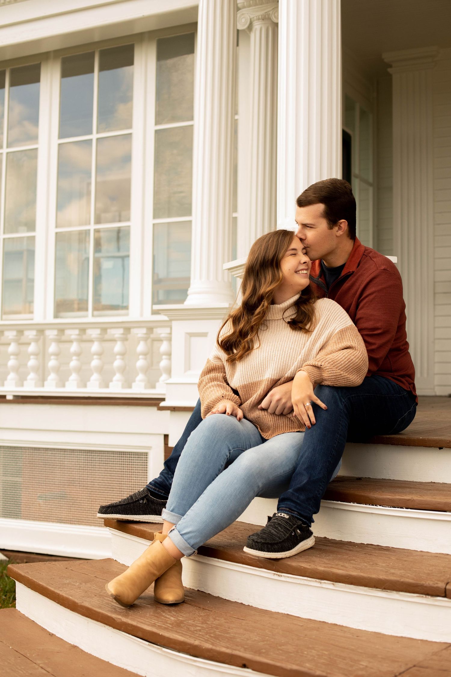 A couple sharing a tender moment while sitting on white porch steps.