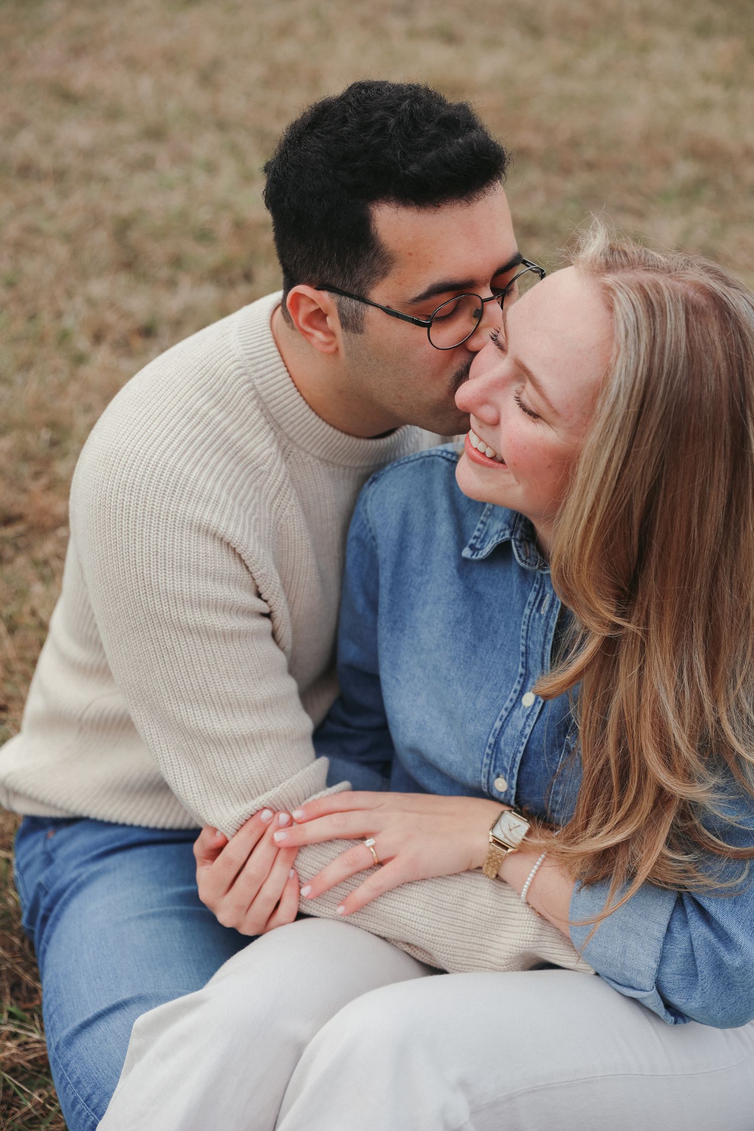 A romantic couple in casual attire shares tender moments while sitting together outdoors.
