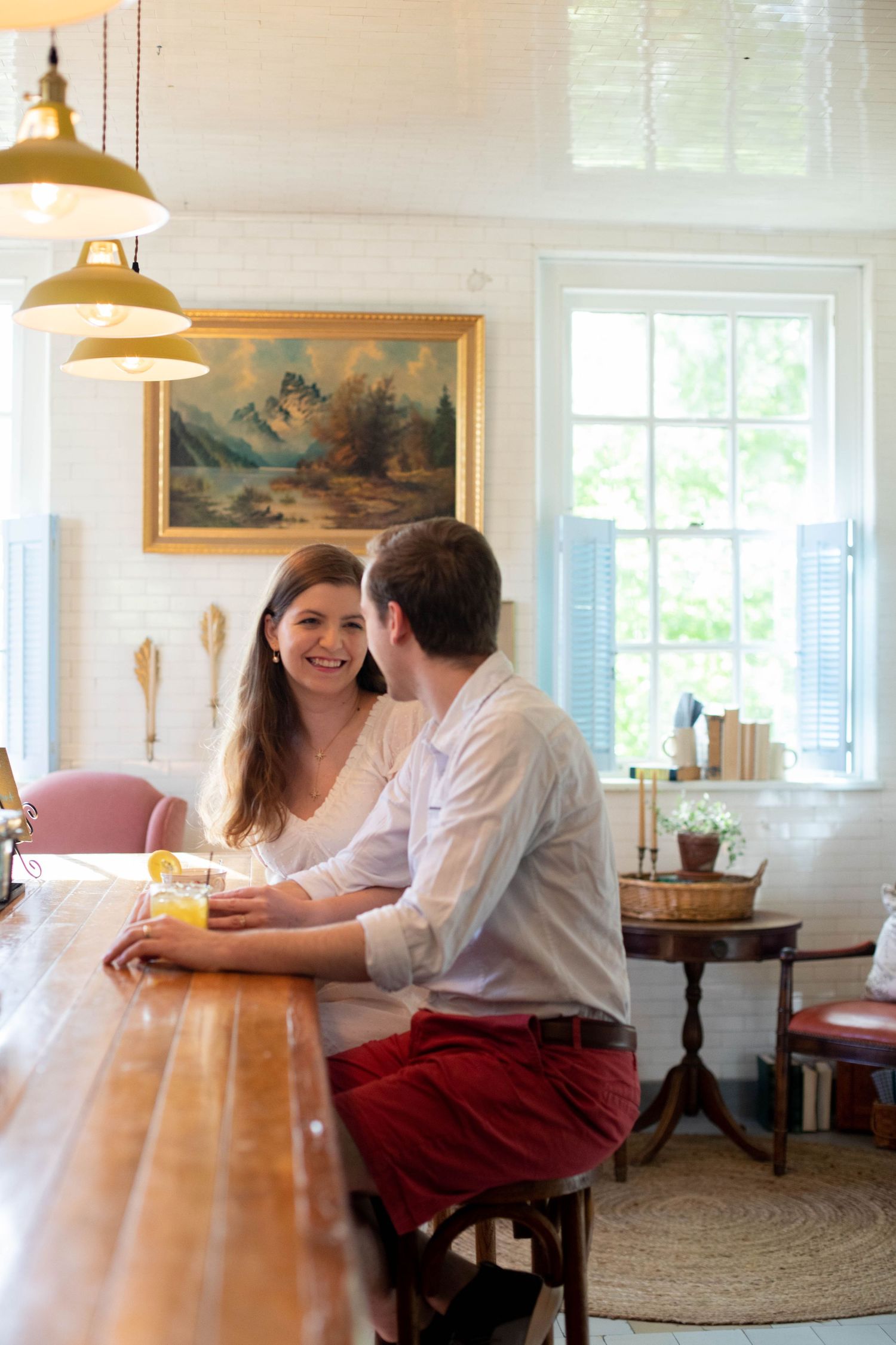 Couple shares tender moments at a bright indoor cafe with pendant lighting.