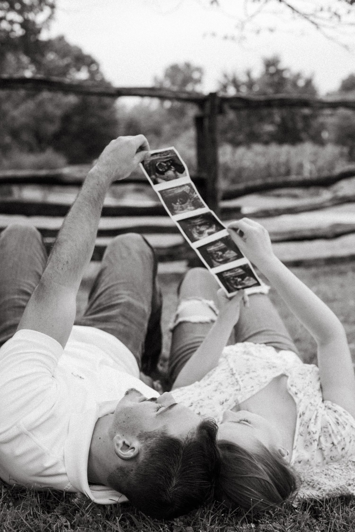 A black and white photo of ultrasound images being held up against a rustic wooden fence.