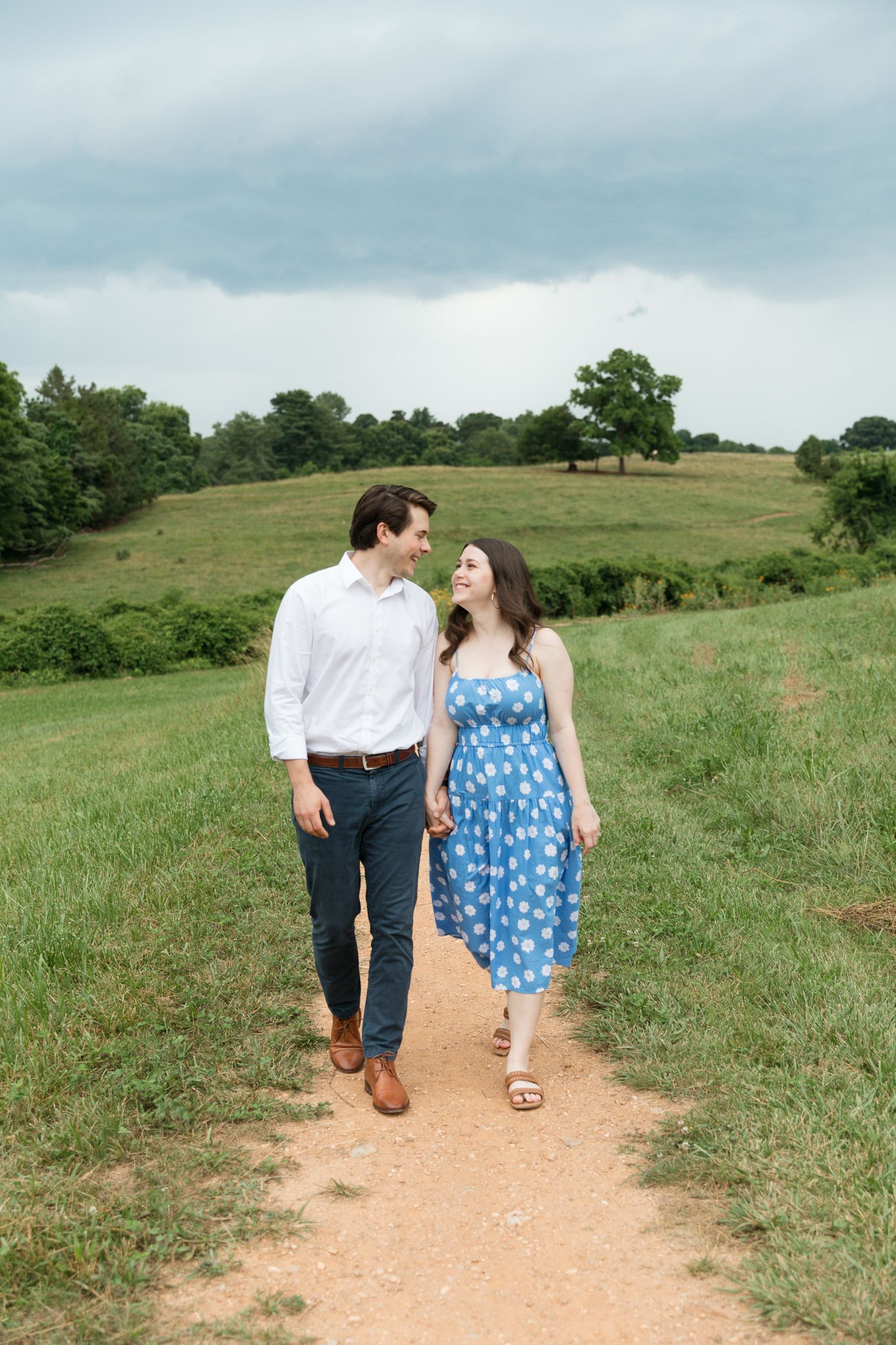 Couple walking hand in hand down a dirt path through rolling green hills.