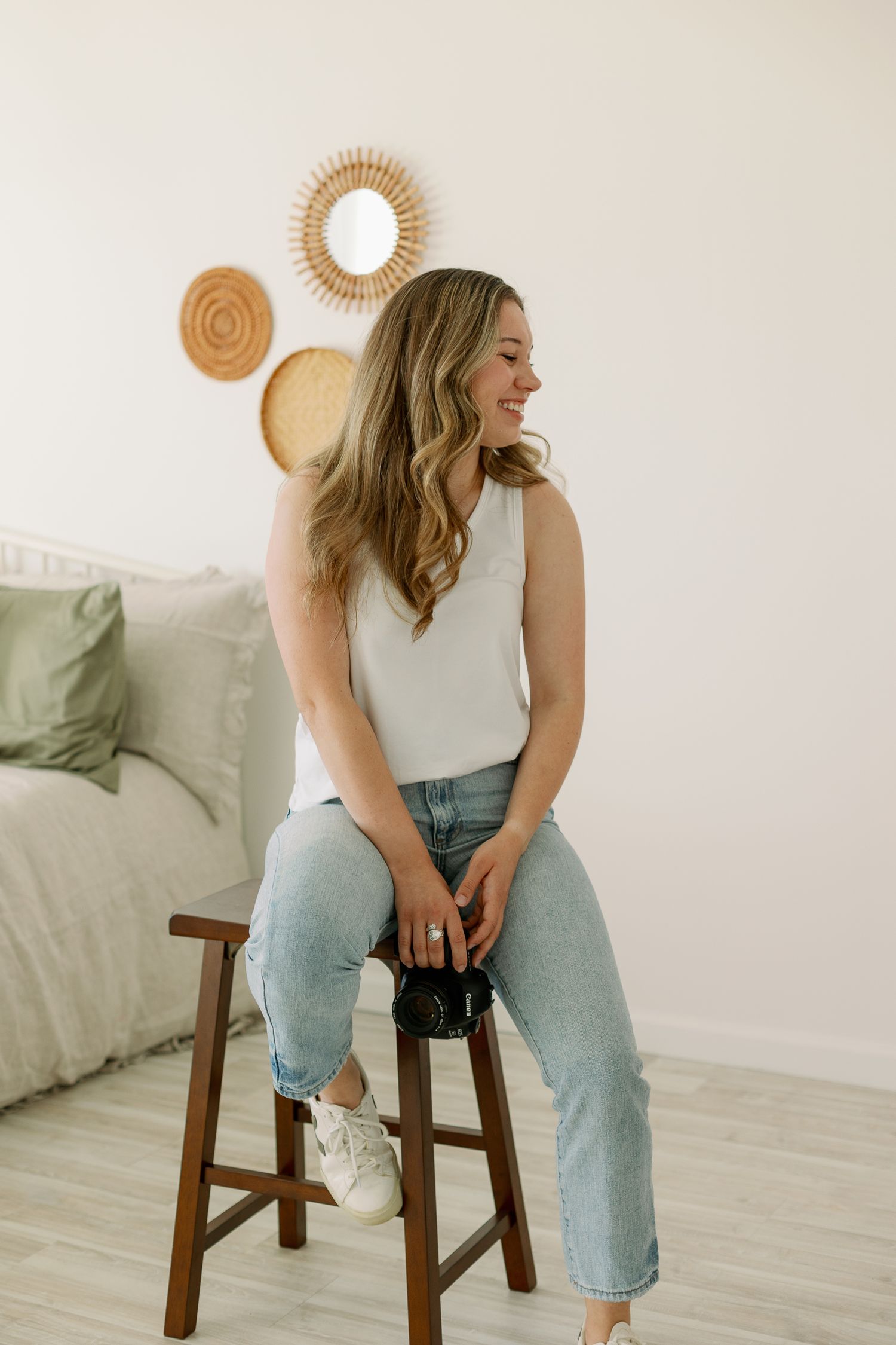 Natural light portrait on wooden stool with rattan wall decor and soft green accents.