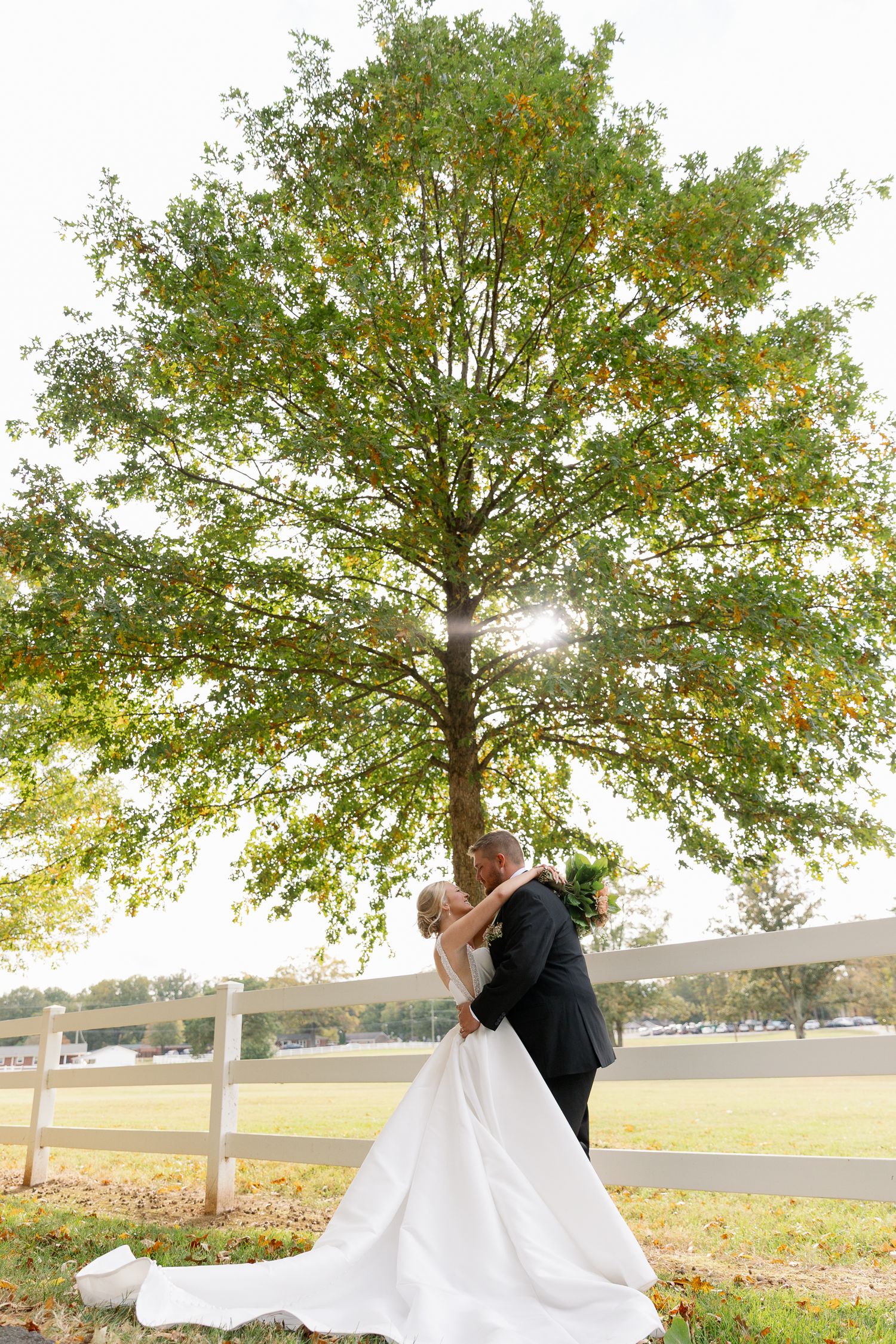 A couple in formal attire embraces under autumn trees in a romantic outdoor wedding photo shoot.