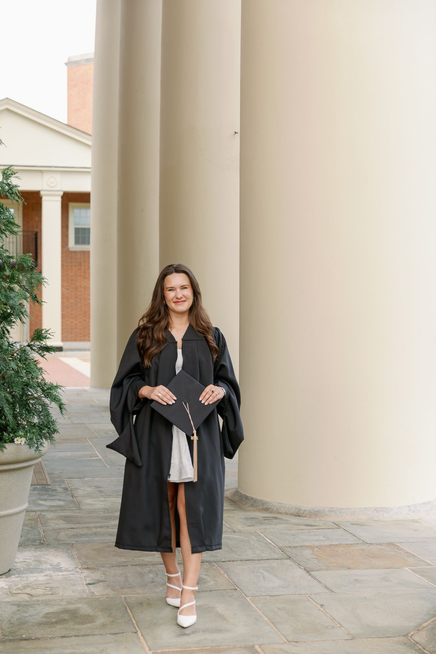 Person posing between white columns wearing black leather jacket and white dress.