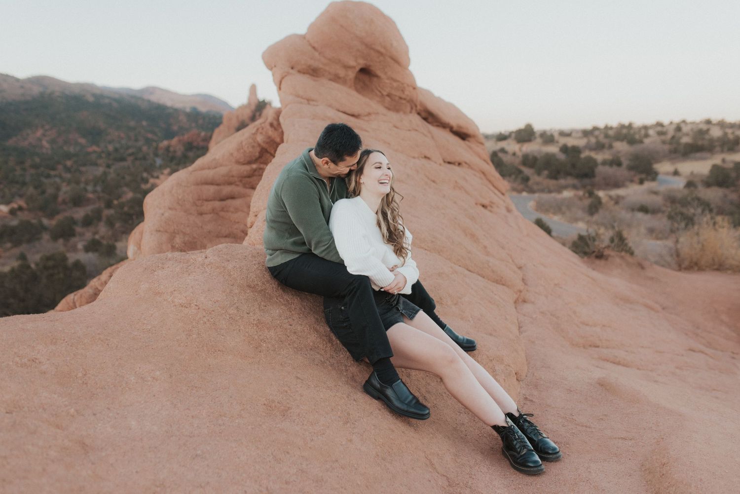 A couple snuggles together on smooth red rocks at Garden of the Gods in Colorado Springs, Colorado