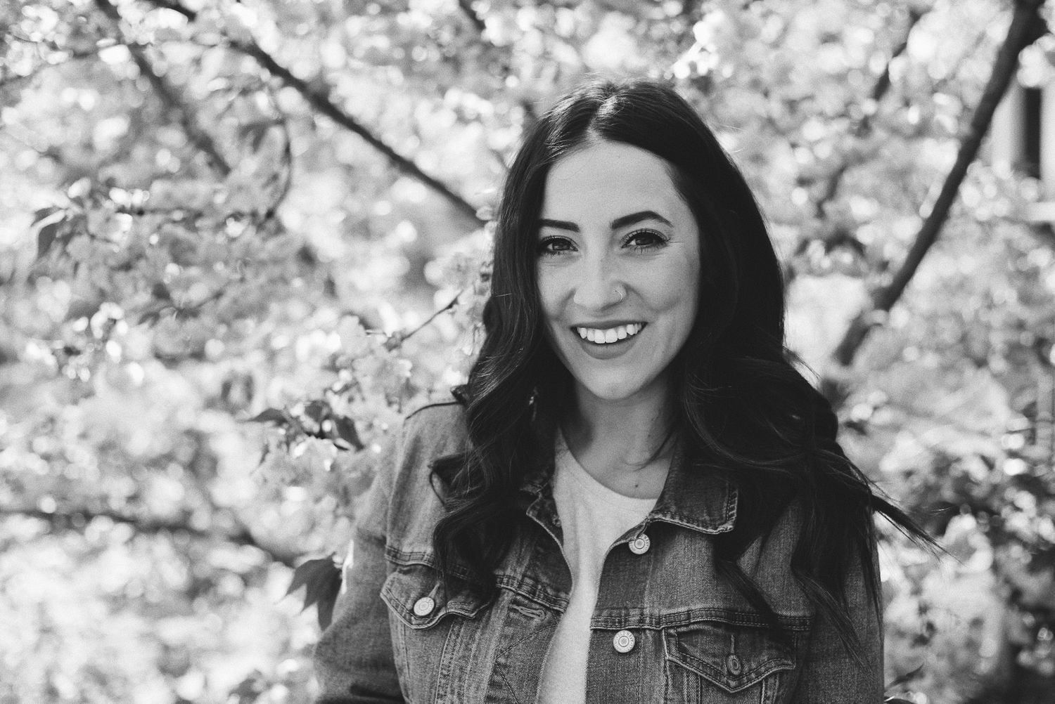 Black and white closeup portrait of woman smiling with long dark hair and denim jacket.