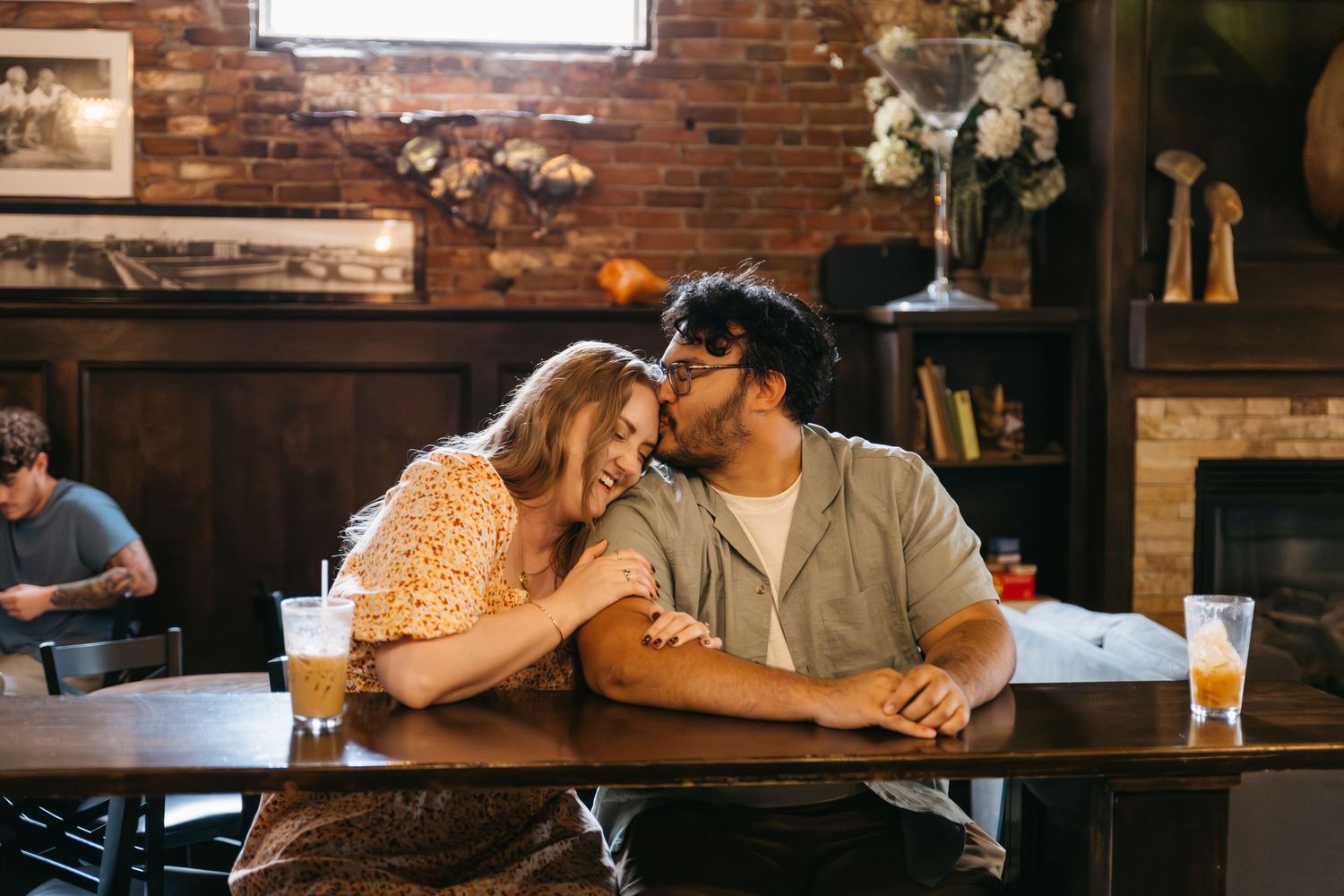 Couple sharing intimate moments at a rustic bar with exposed brick walls and warm lighting in background.