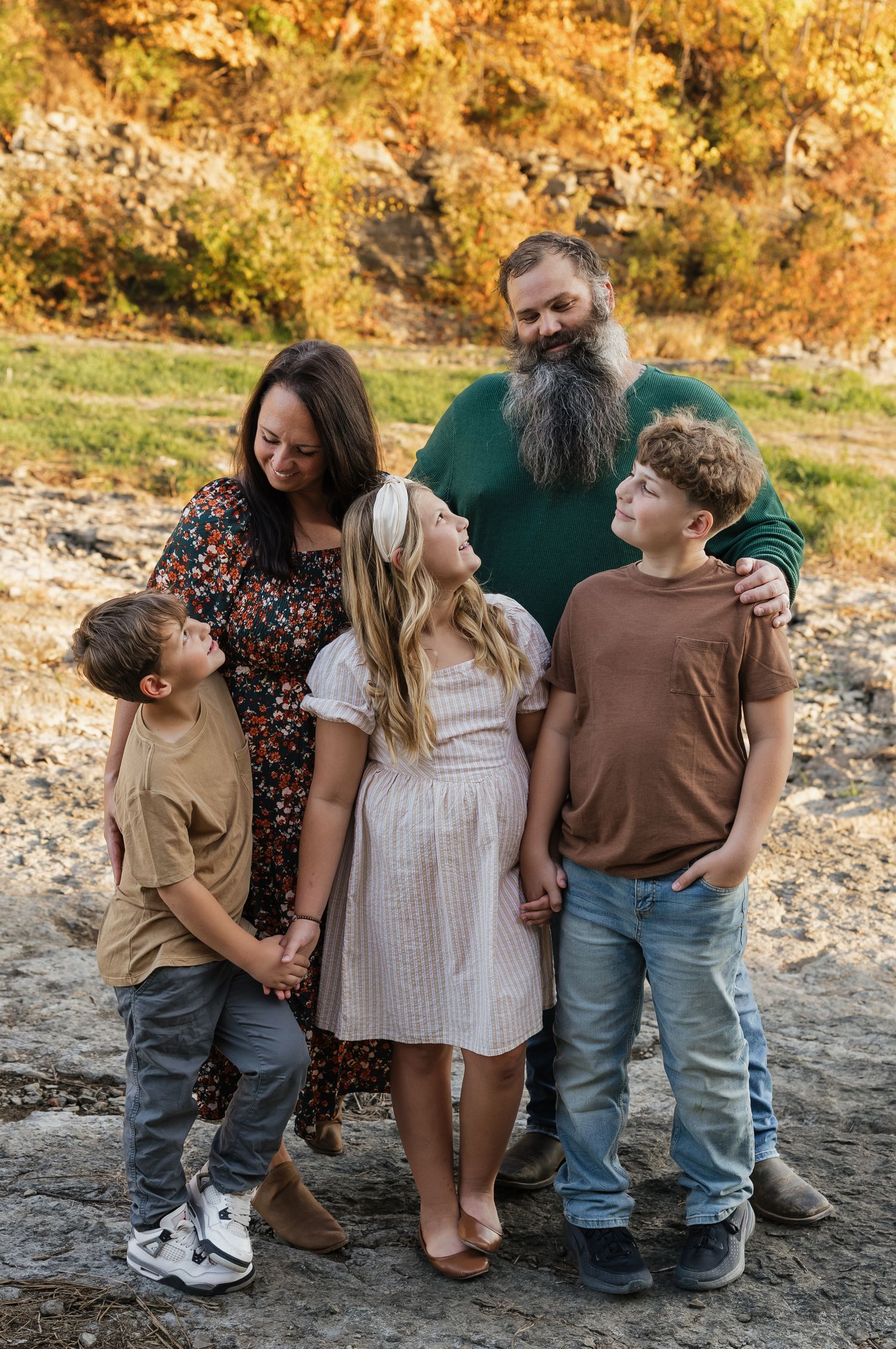 Family group poses together on rocky terrain during golden sunset photoshoot.