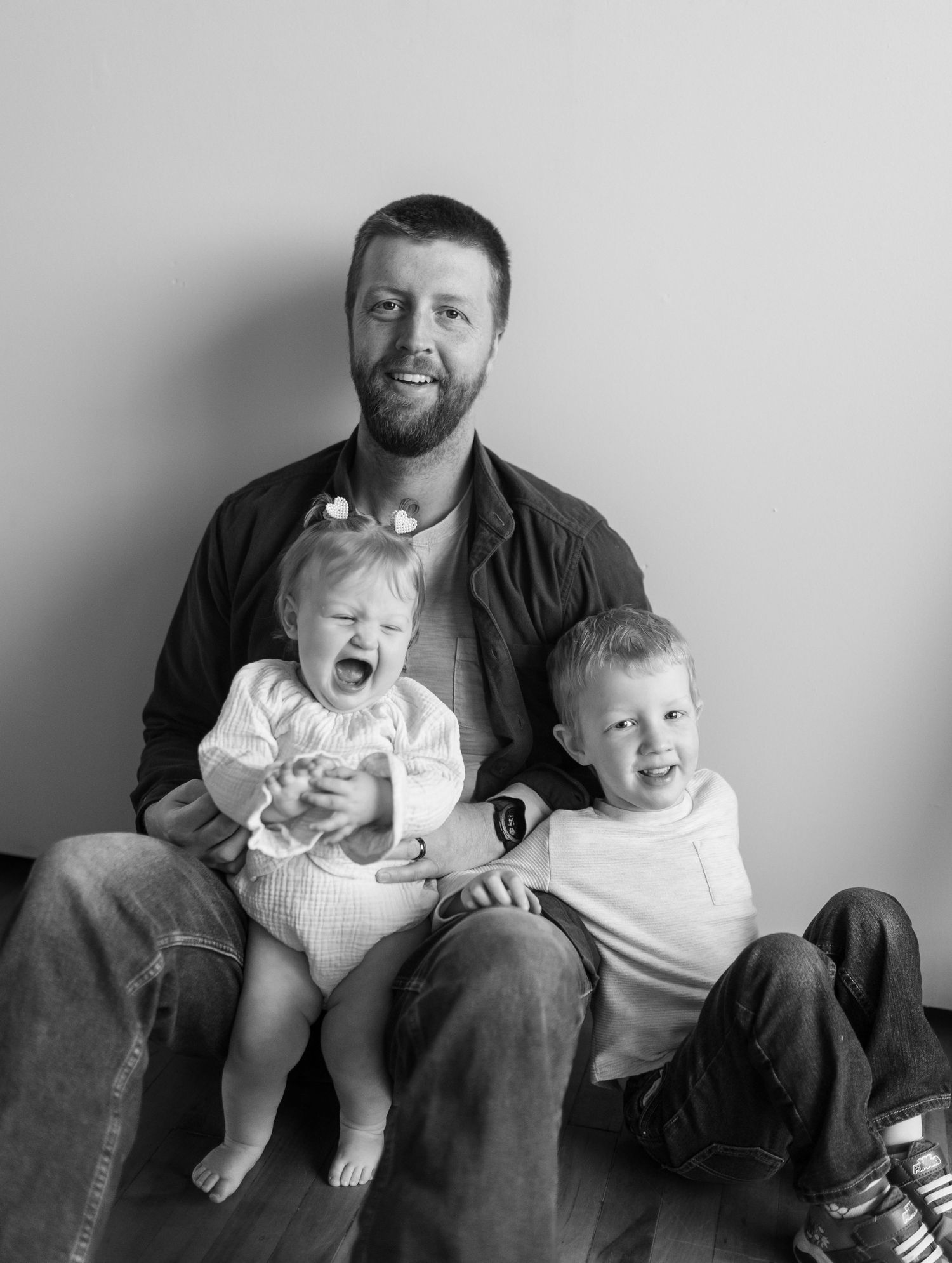 A black and white portrait of a parent with two children showing various expressions.